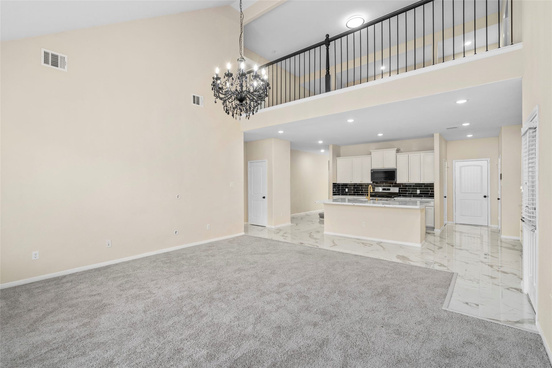 9423 Mineral Rock Lane, Richmond, TX 77407 Expansive living room featuring soaring ceilings, plush carpeting, and a stunning chandelier, seamlessly flowing into a modern kitchen with sleek finishes and a stylish balcony overlook.