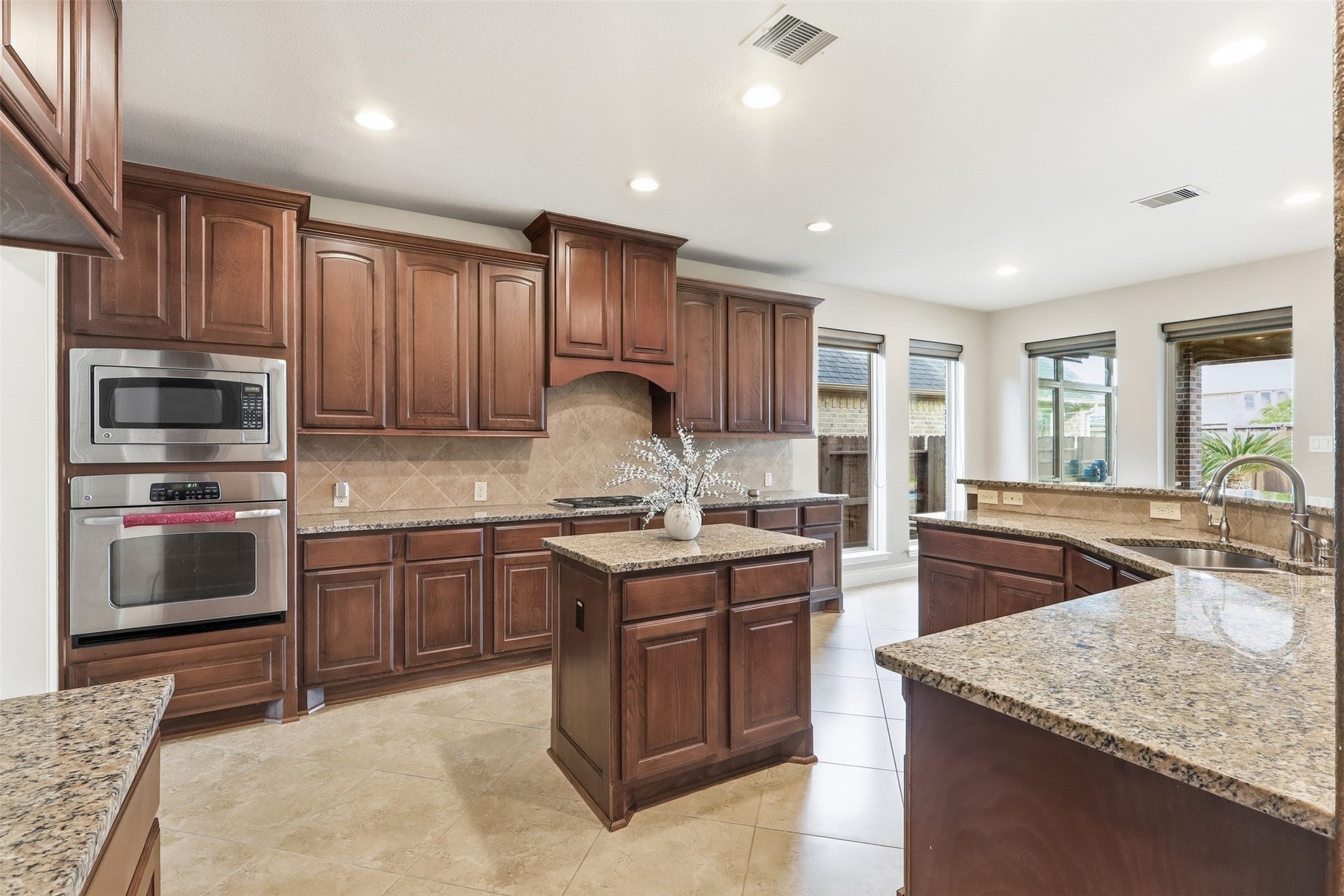 4130 Clover Ridge Lane, Sugar Land, TX 77479 This kitchen features elegant dark wood cabinetry, granite countertops, and a central island. It includes stainless steel appliances and ample natural light from large windows.