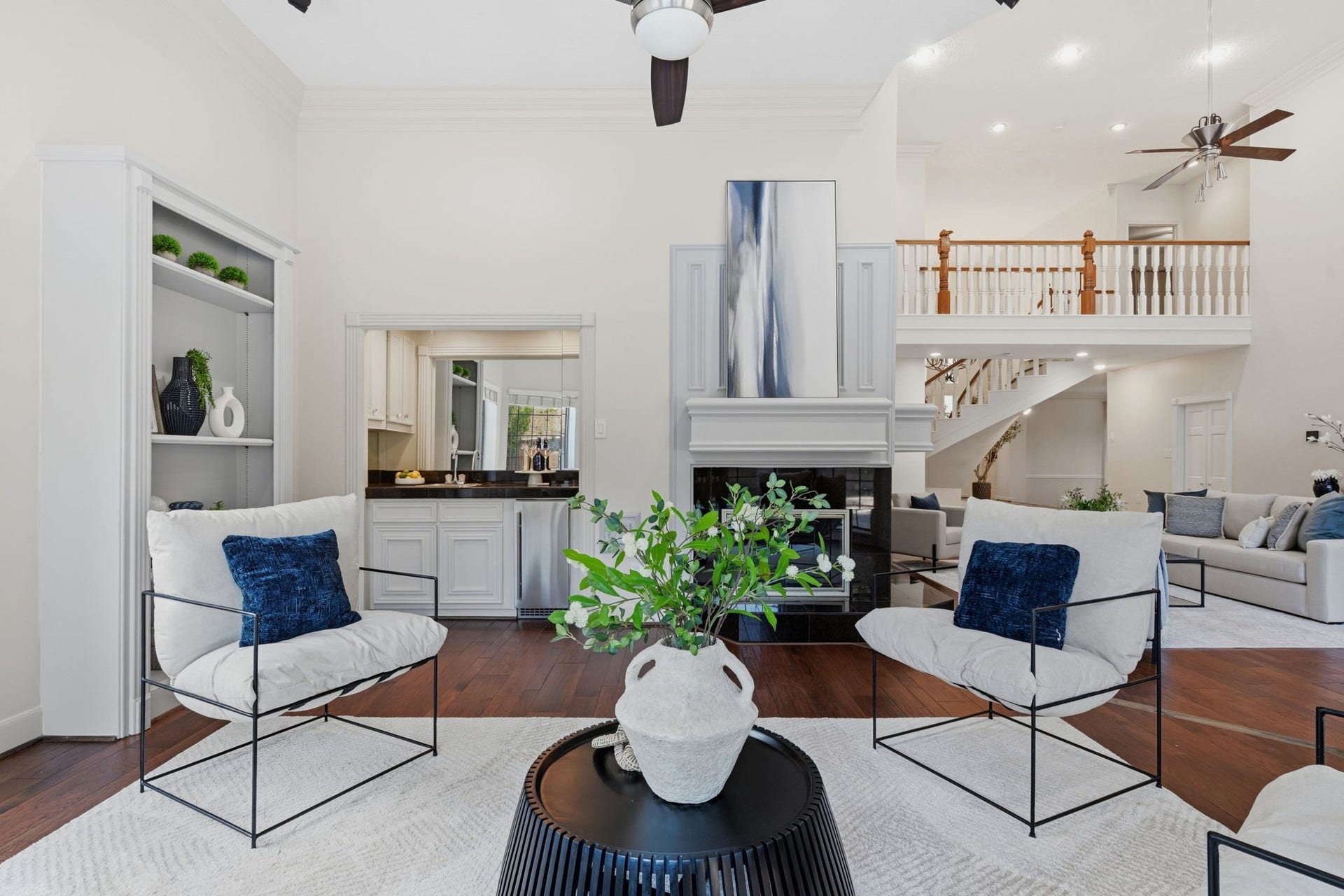 This beautiful perspective of the formal living room highlights custom built-in shelving with elegant millwork & a convenient wet bar, adding both sophistication & functionality. An impressive double-sided fireplace serves as a striking architectural focal point, seamlessly connecting the home's spacious living areas.