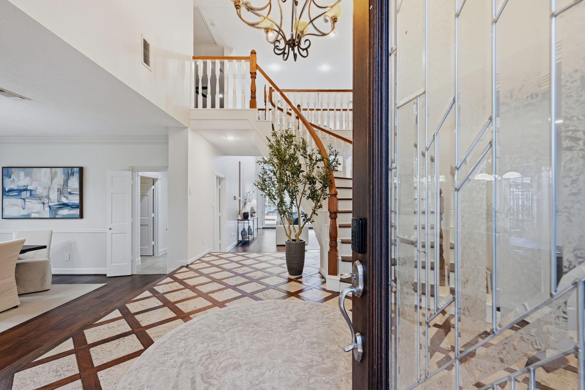 Step inside to discover a breathtaking two-story foyer, where an elegant curved staircase with rich hardwood treads & contrasting white spindles create a stunning focal point. A striking chandelier illuminates the beautifully patterned flooring below, while the open design offers inviting glimpses into this gorgeous home.