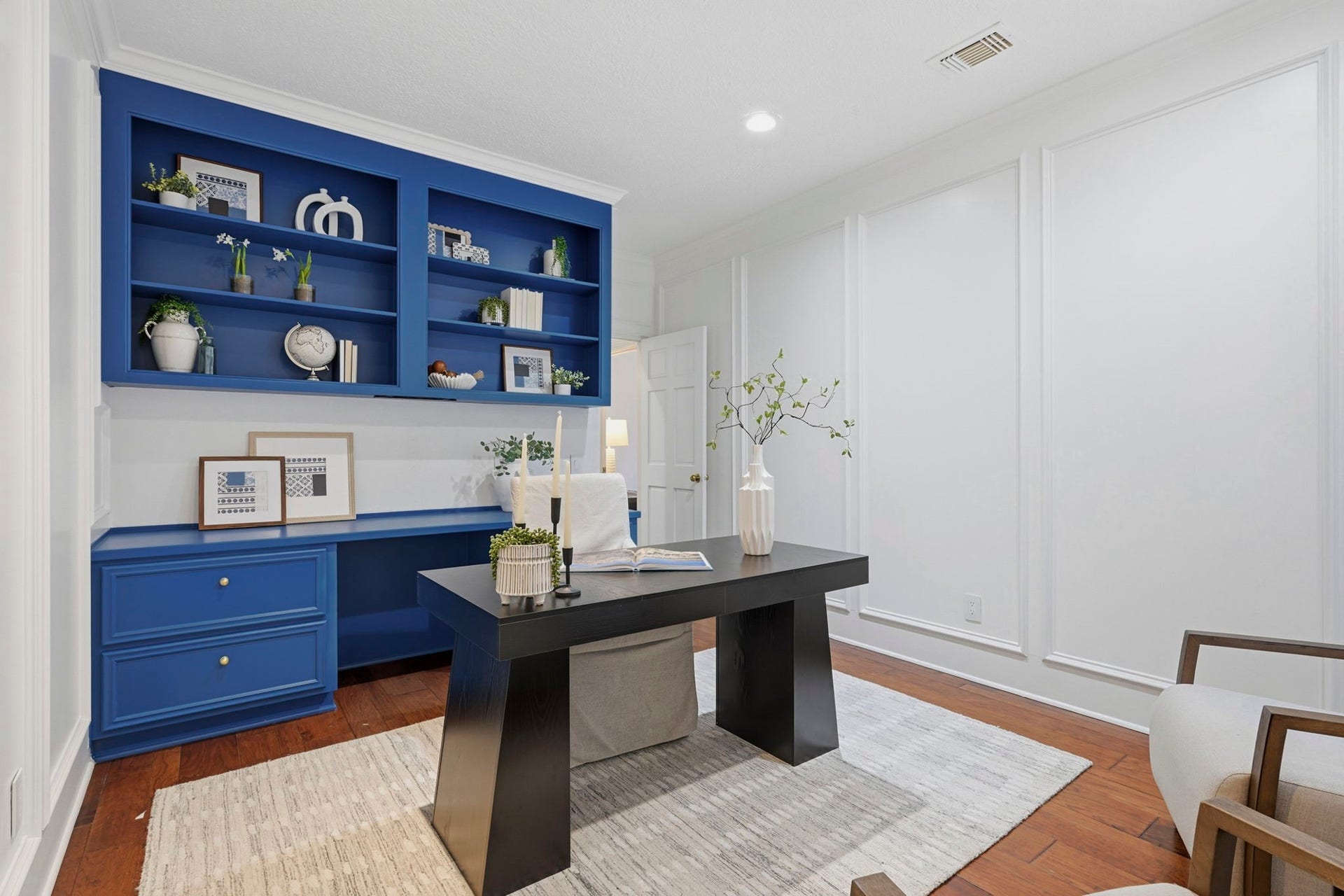 This beautifully appointed study offers a sophisticated workspace featuring rich hardwood flooring, crisp white walls, & a striking custom built-in desk with a vibrant blue finish. Recessed lighting, elegant moldings, & generous proportions complete this thoughtfully designed room.