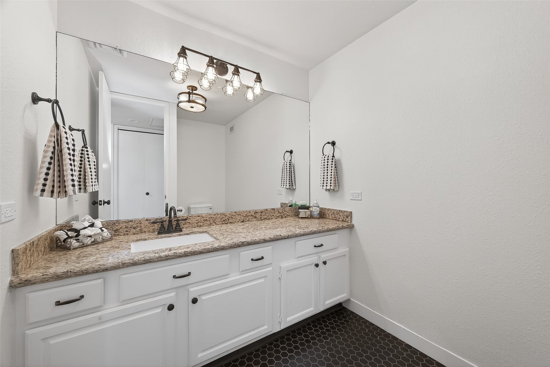 2016 Main Street, #PH 3, Houston, TX 77002 Elegant bathroom featuring a spacious granite countertop with ample cabinet storage, accented by chic lighting and a large mirror, creating a bright and inviting space.