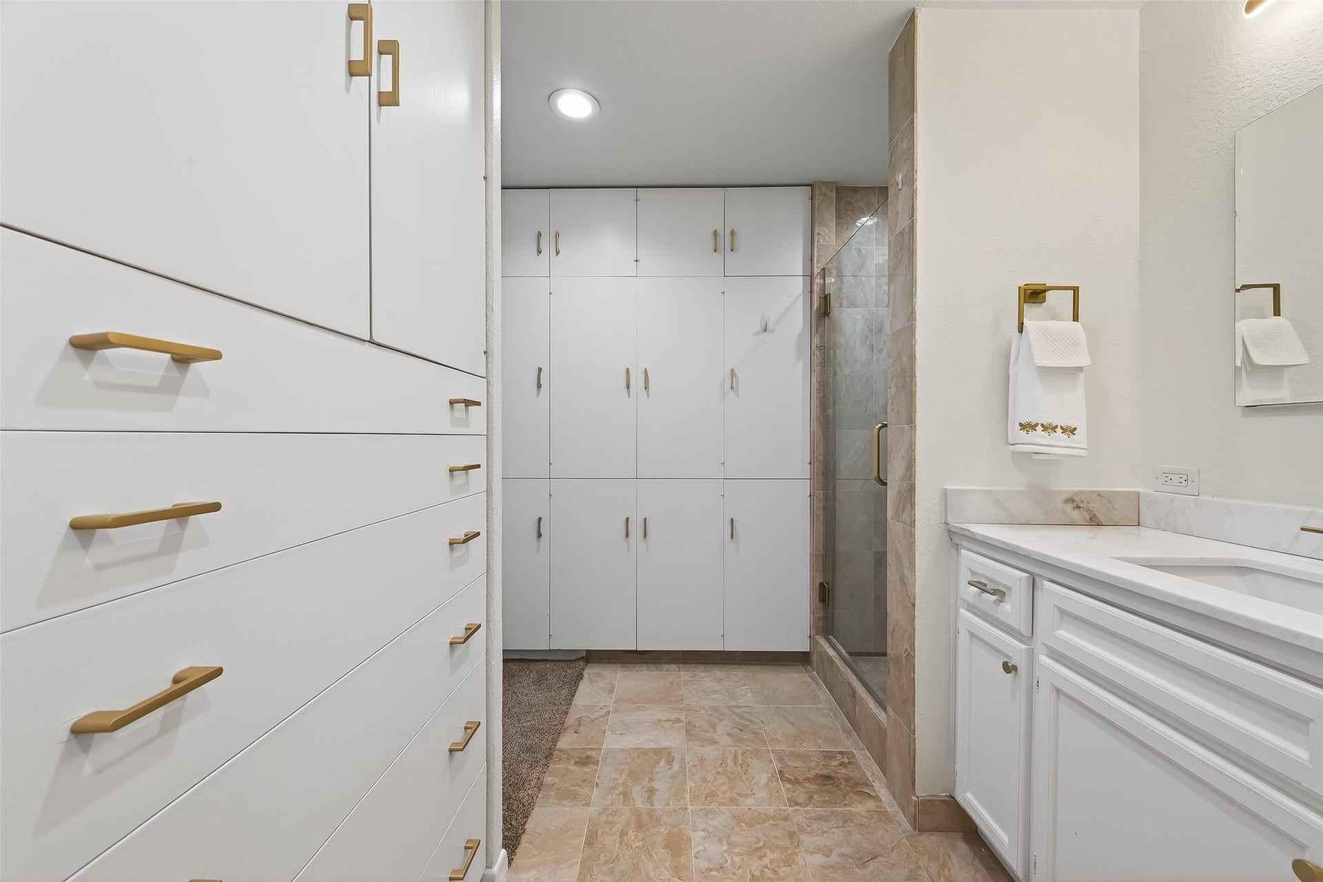 2016 Main Street, #PH 3, Houston, TX 77002 Elegant bathroom featuring ample storage with sleek white cabinetry and brass hardware, complemented by a luxurious marble countertop and a glass-enclosed shower.