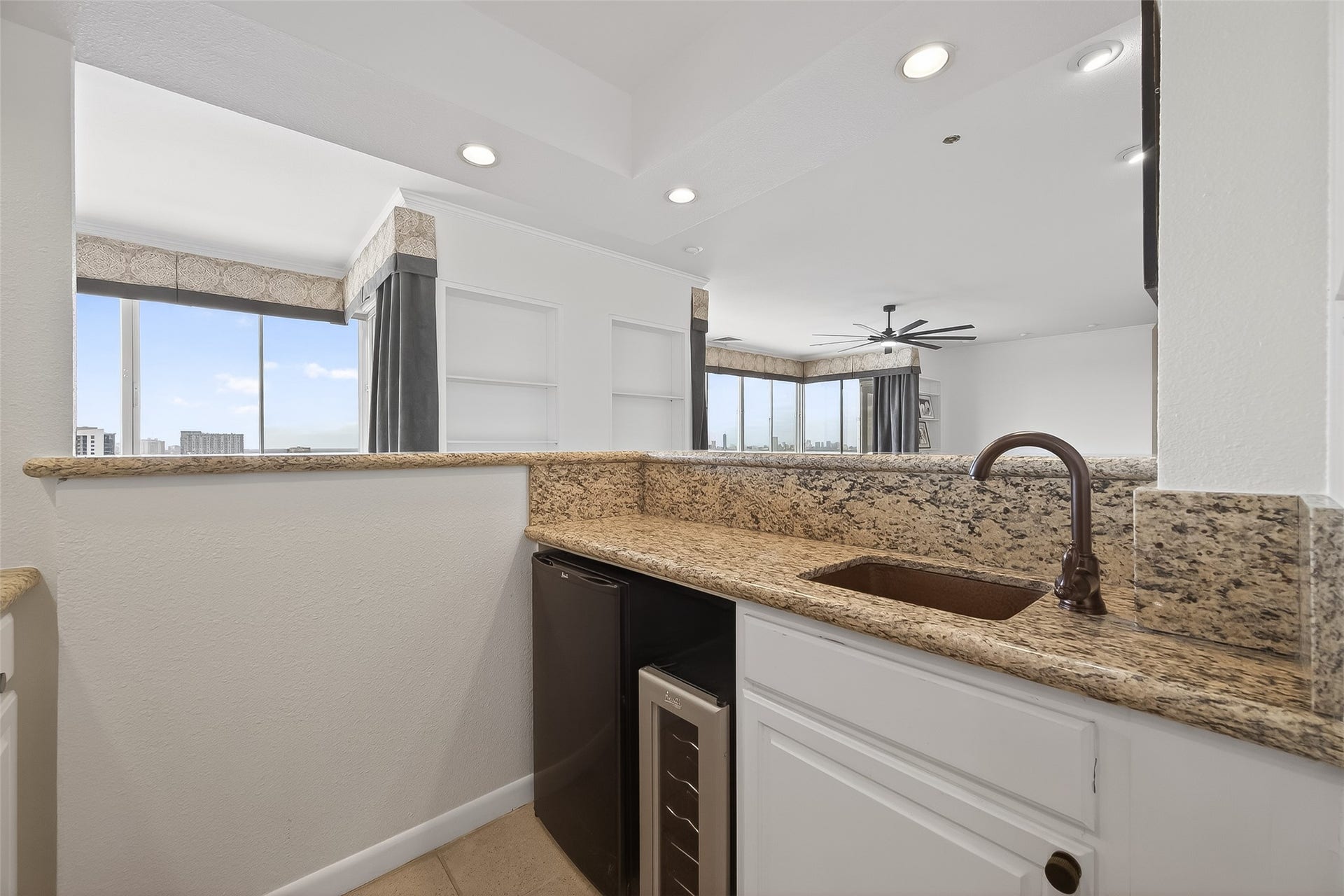 2016 Main Street, #PH 3, Houston, TX 77002 Stylish wet bar area featuring elegant granite countertops, a sleek under-counter wine fridge, and a modern sink, seamlessly opening to a bright living space with expansive city views.