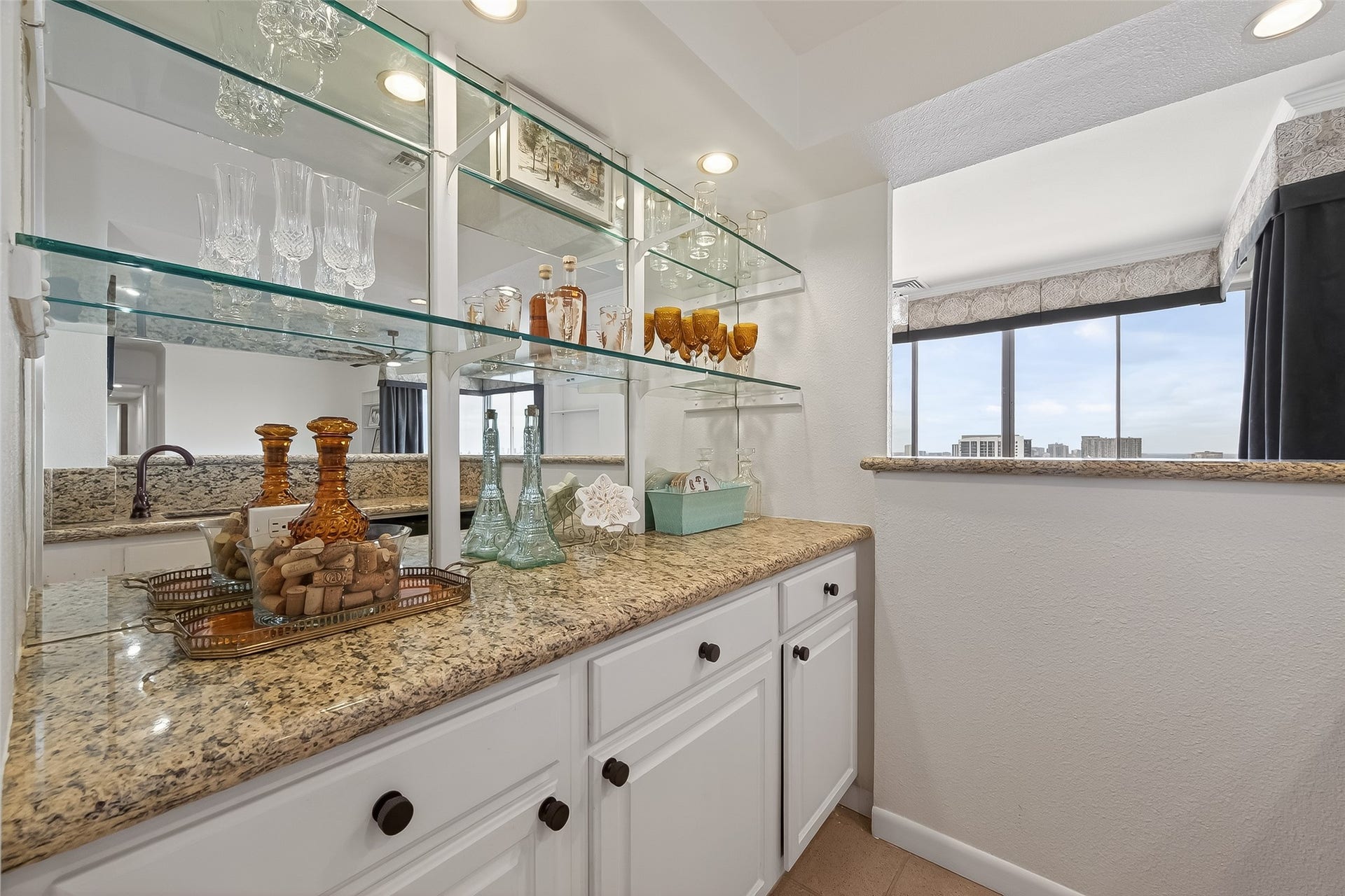 2016 Main Street, #PH 3, Houston, TX 77002 Elegant wet bar with sleek granite countertops, ample cabinet storage, and glass shelves displaying crystal glassware, perfect for entertaining.