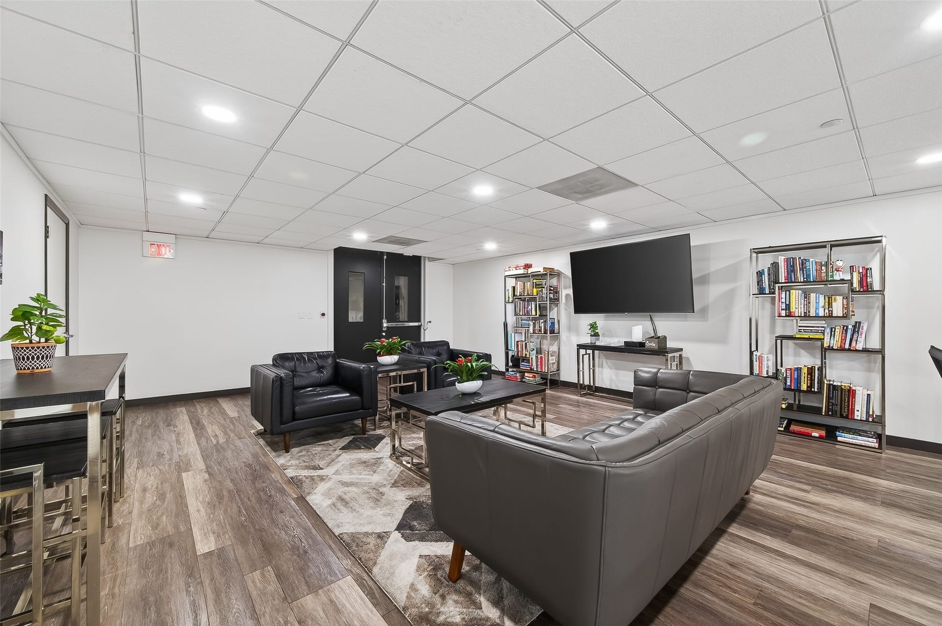 2016 Main Street, #PH 3, Houston, TX 77002 Spacious modern lounge area featuring sleek black leather seating, a large wall-mounted TV, stylish bookshelves, and contemporary decor, perfect for relaxation and entertainment.