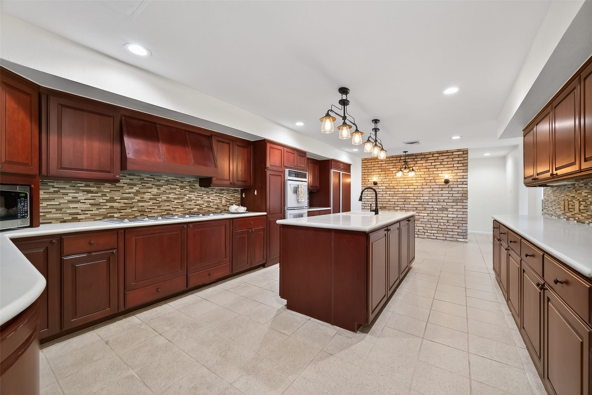 2016 Main Street, #PH 3, Houston, TX 77002 Spacious kitchen featuring rich wood cabinetry, a large central island with modern lighting, and elegant tile backsplash, perfect for culinary enthusiasts.