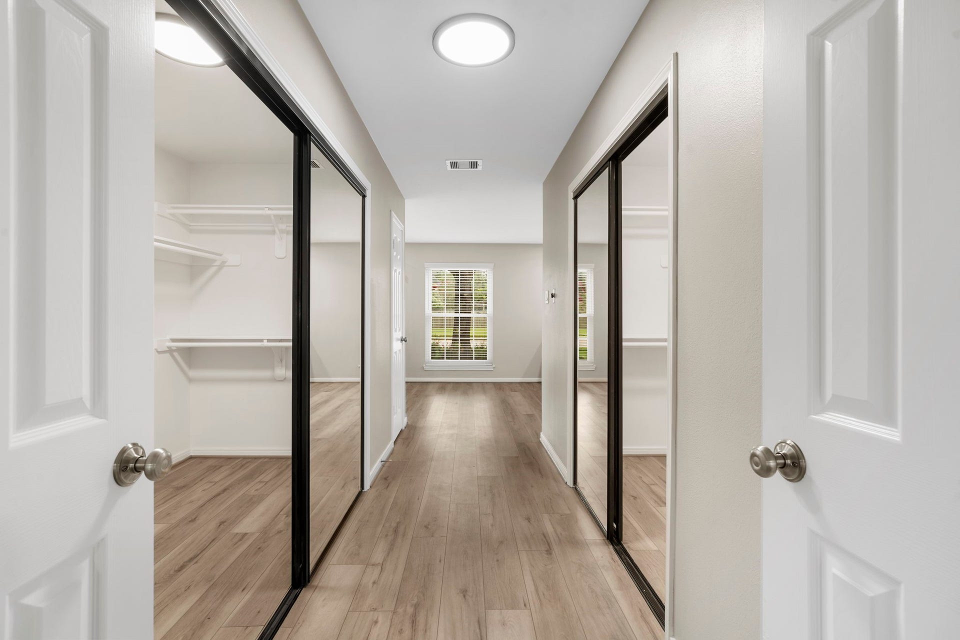 A spacious dressing area connects the primary suite & bath, offering dual closets with mirrored doors and abundant storage on both sides.