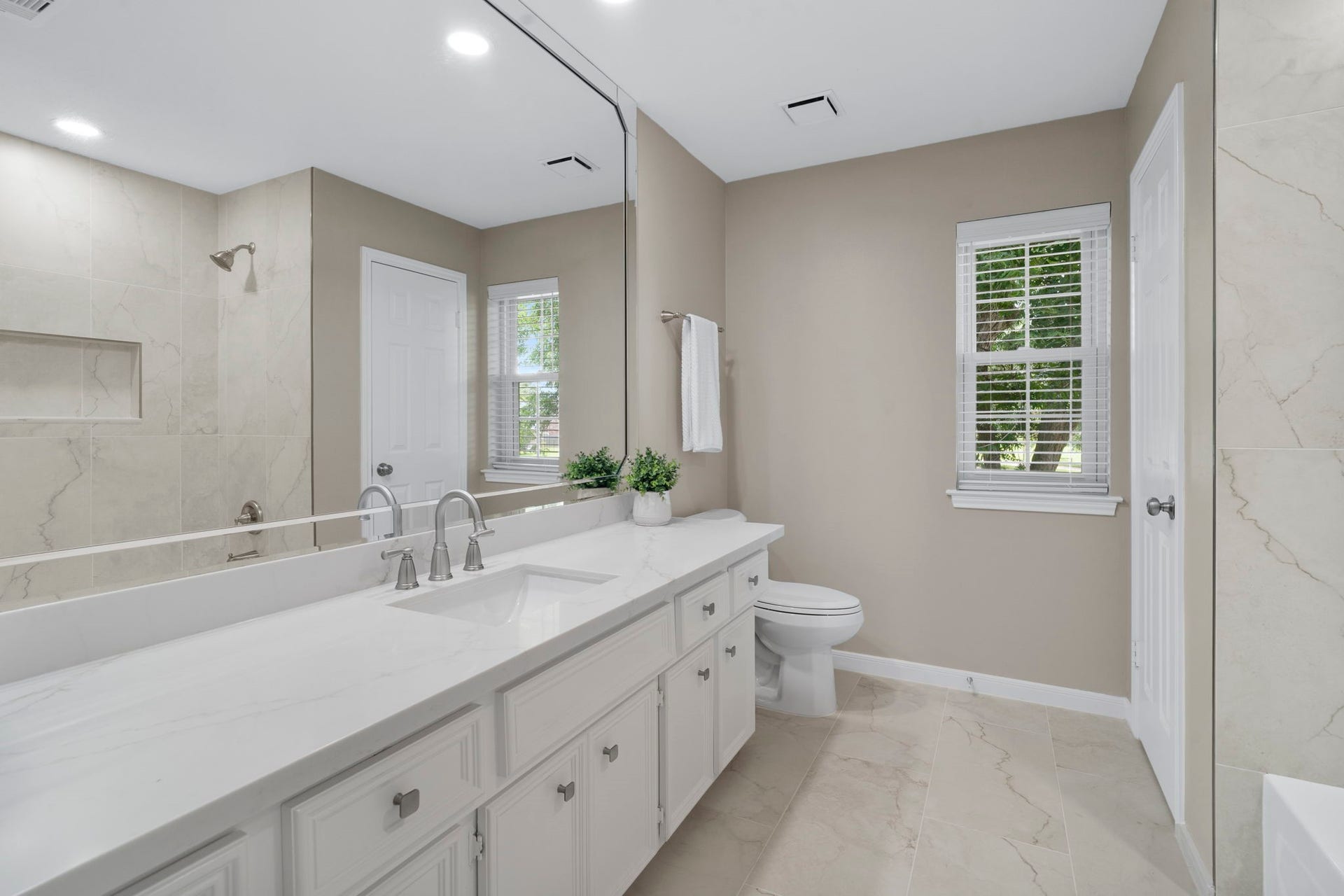 The updated secondary bath features a long vanity quartz countertop and expansive mirror.