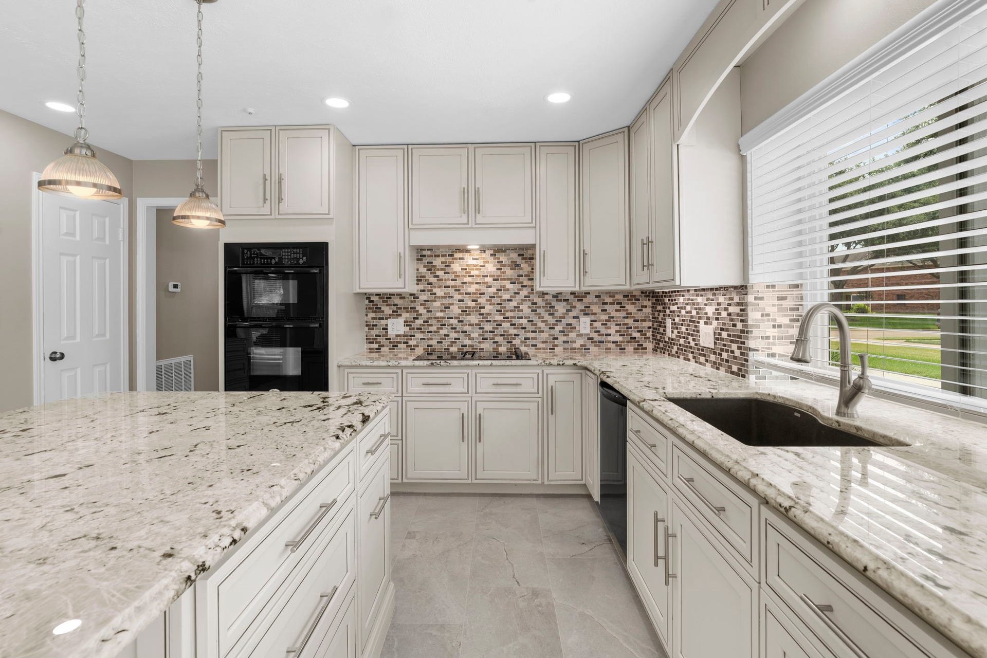 The kitchen offers abundant cabinetry, generous counter space & a large center island, complemented by granite surfaces, a mosaic tile backsplash & updated lighting. A large window over the sink fills the space with natural light.