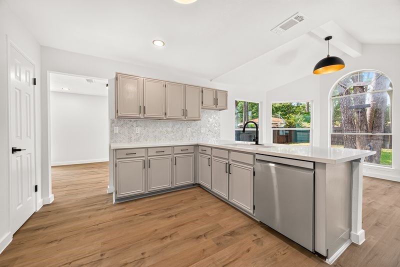 Bright and modern kitchen featuring sleek gray cabinetry, a stylish backsplash, and stainless steel appliances, complemented by warm wood flooring and ample natural light from large windows.