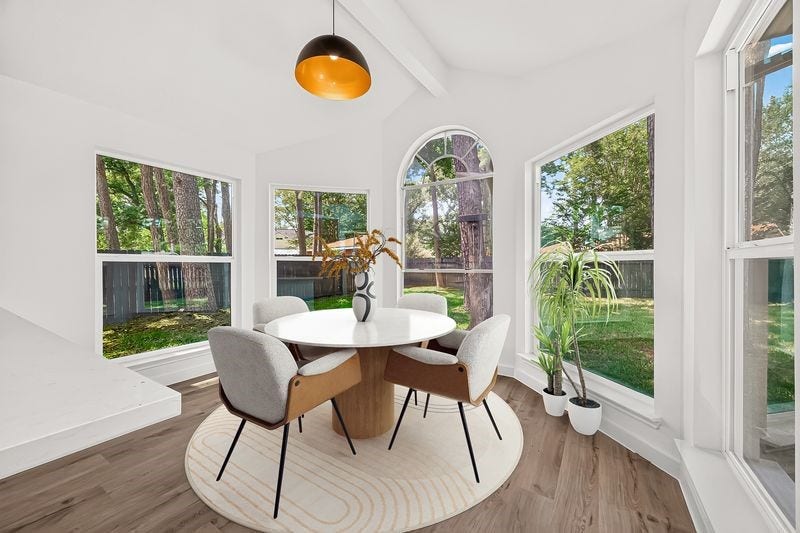Bright dining area with large windows offering scenic views, featuring a modern round table and stylish chairs, accented by a contemporary light fixture.