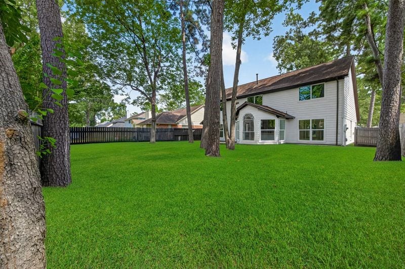 Expansive backyard with lush green lawn and mature trees, perfect for outdoor activities and relaxation, complements this charming two-story home.