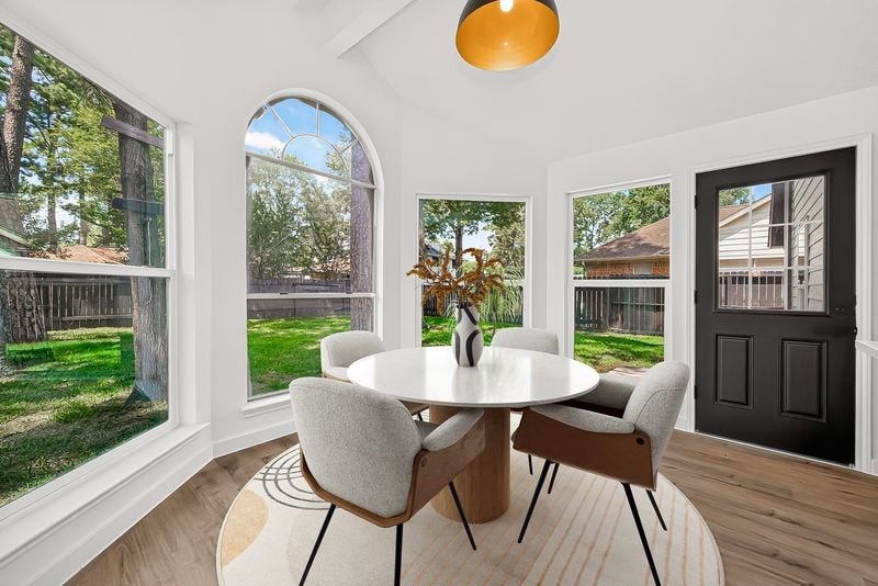 Bright and airy dining nook featuring large windows with serene garden views, a cozy round table with modern chairs, and a stylish light fixture.