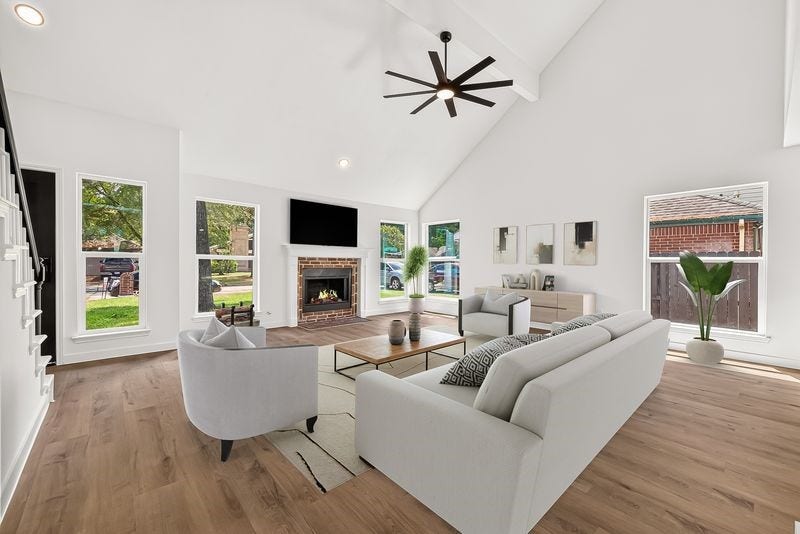 Spacious living room with vaulted ceilings, abundant natural light, and a cozy brick fireplace, perfect for relaxing or entertaining.