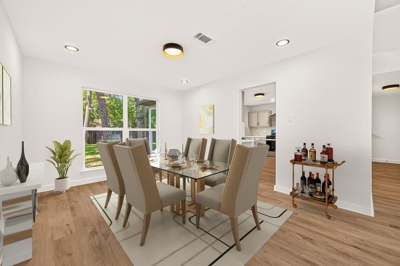 Bright and spacious dining room featuring elegant wood flooring, large windows with a view of the lush backyard, and seamless access to the modern kitchen.