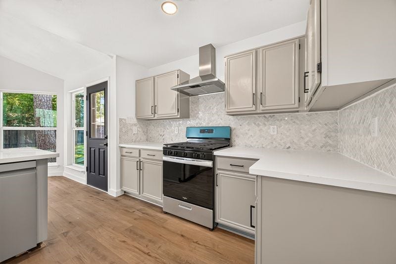 Bright and spacious kitchen featuring modern stainless steel appliances, sleek cabinetry, and elegant herringbone backsplash, all complemented by warm wood flooring and abundant natural light.