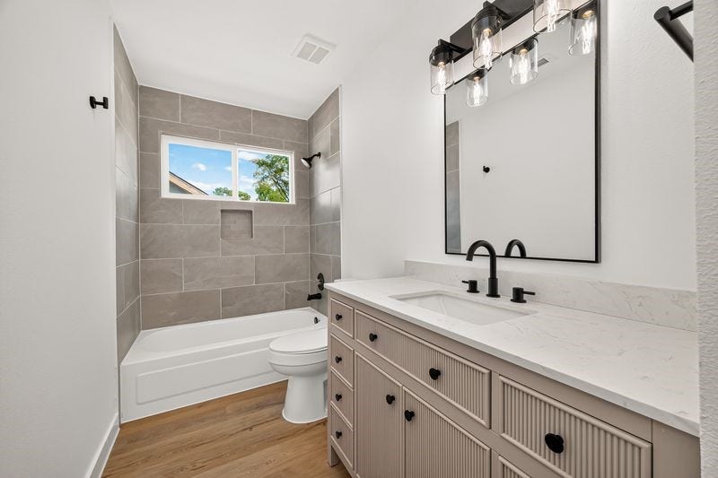 Elegant bathroom featuring a modern vanity with marble countertop, stylish fixtures, and a chic tub with gray tile surround.