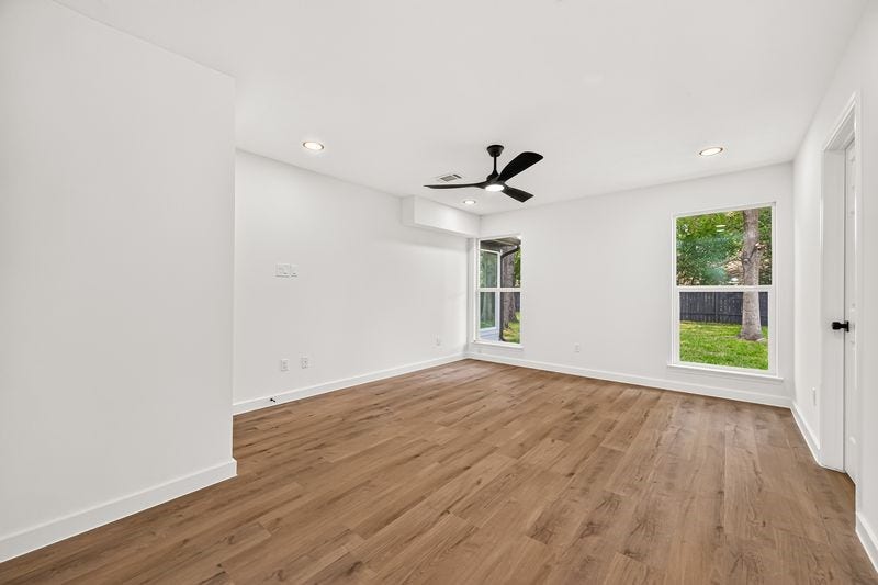 Bright and airy living space featuring sleek hardwood floors, modern ceiling fan, and large windows offering lush views of the backyard.
