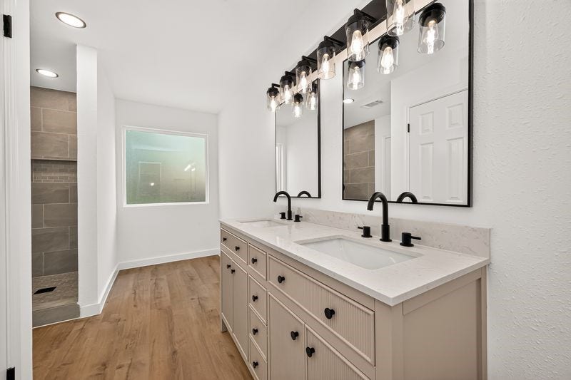 Elegant bathroom with a double vanity, sleek black fixtures, and modern lighting. The spacious shower and warm wood flooring add a touch of luxury.