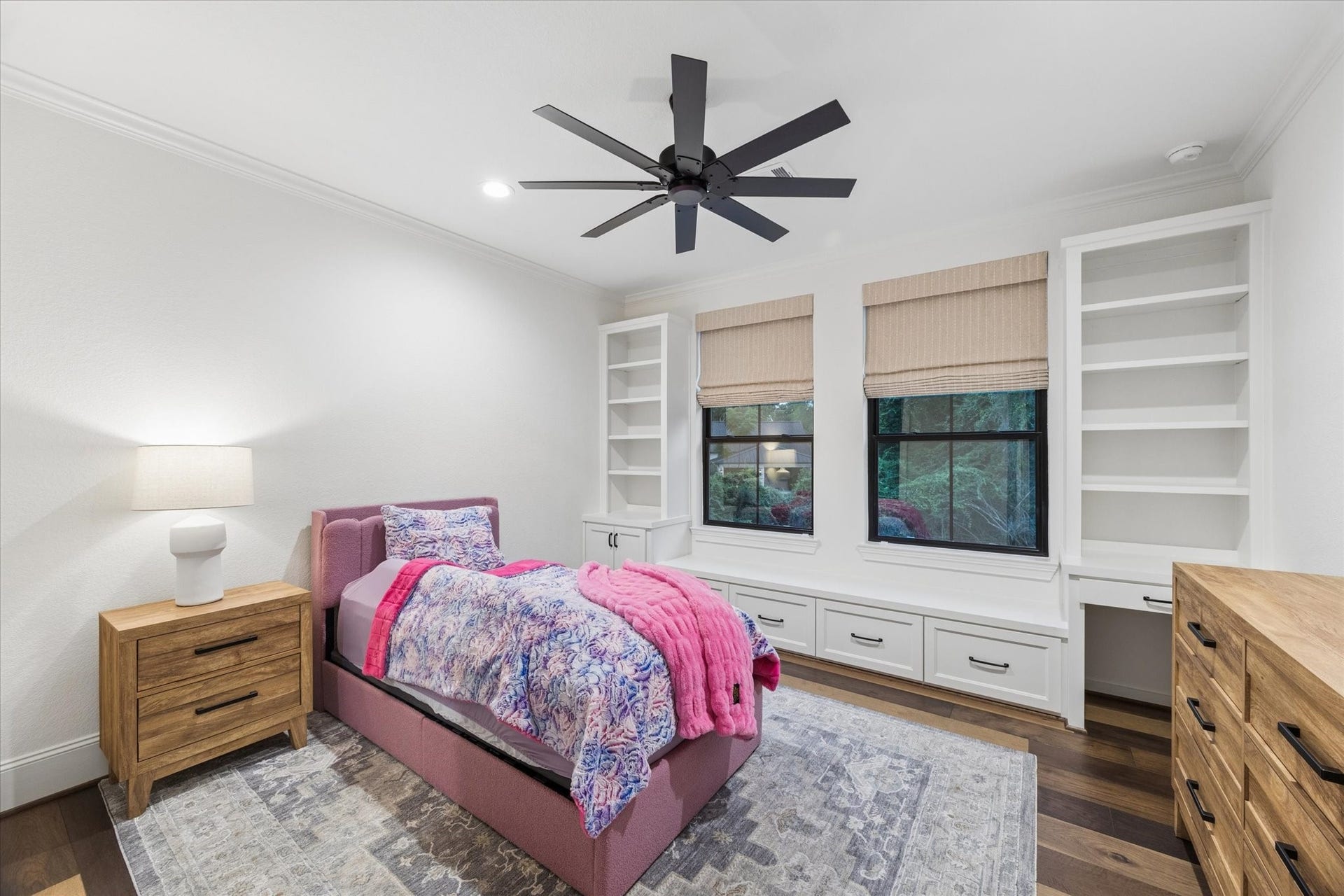 Comfort and craftsmanship define this inviting secondary bedroom. Custom carpenter-built shelving, integrated seating, and abundant natural light create a warm and highly functional retreat.