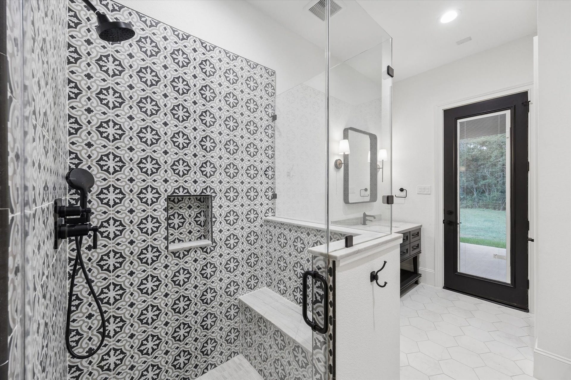 The full pool bathroom provides convenient access from both the interior and the covered patio, making it ideal for future pool use and outdoor entertaining. A striking patterned shower wall creates a dramatic designer focal point, while the walk-in shower includes built-in niches and carefully selected fixtures. Clean architectural lines, abundant natural light, and direct exterior access combine style and practicality in a space thoughtfully designed to support the homes indoor-outdoor lifestyle.