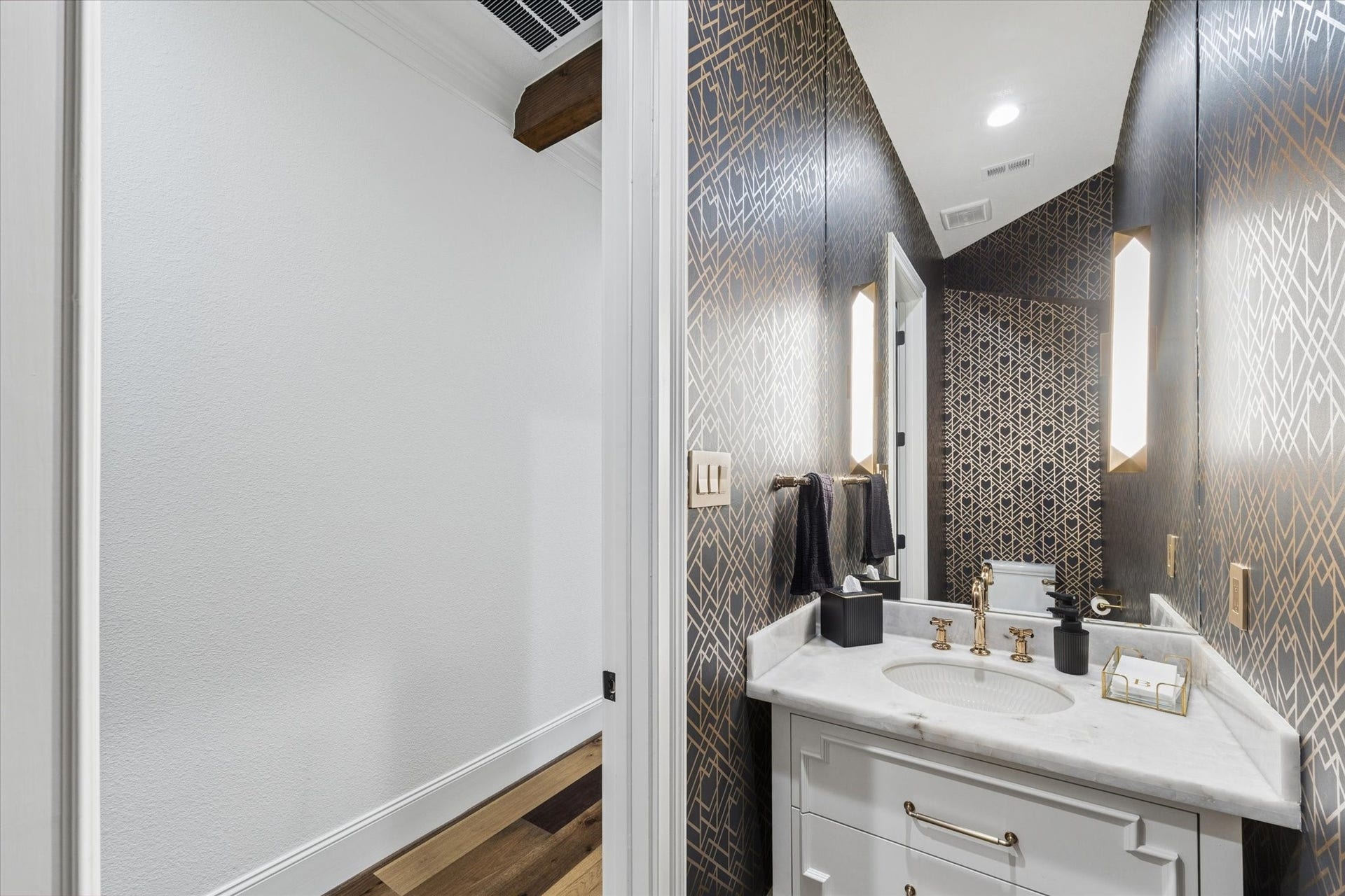 The dramatic powder bath makes a memorable impression with its sophisticated jewel-box design. Full custom wallpaper surrounds the space with rich pattern and dimension, while a floating custom vanity topped with marble adds modern elegance. A full-height mirror extending toward the ceiling, designer sconces, and thoughtfully coordinated finishes create a refined guest experience. Every element reflects the homes commitment to distinctive materials and elevated craftsmanship.