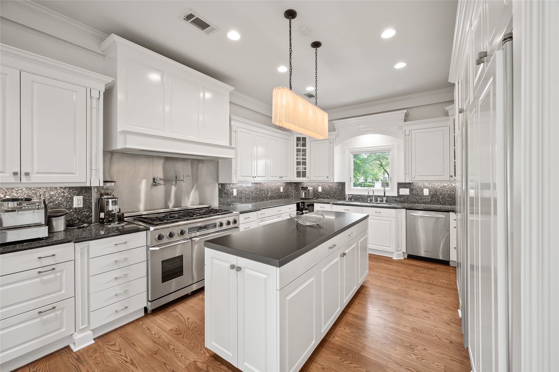 [Gathering Kitchen]
Select granite countertops and backsplash contrast beautifully with white cabinetry. Note under-counter lighting, Dacor range with ovens, and stainless steel range-back with pot-filler.