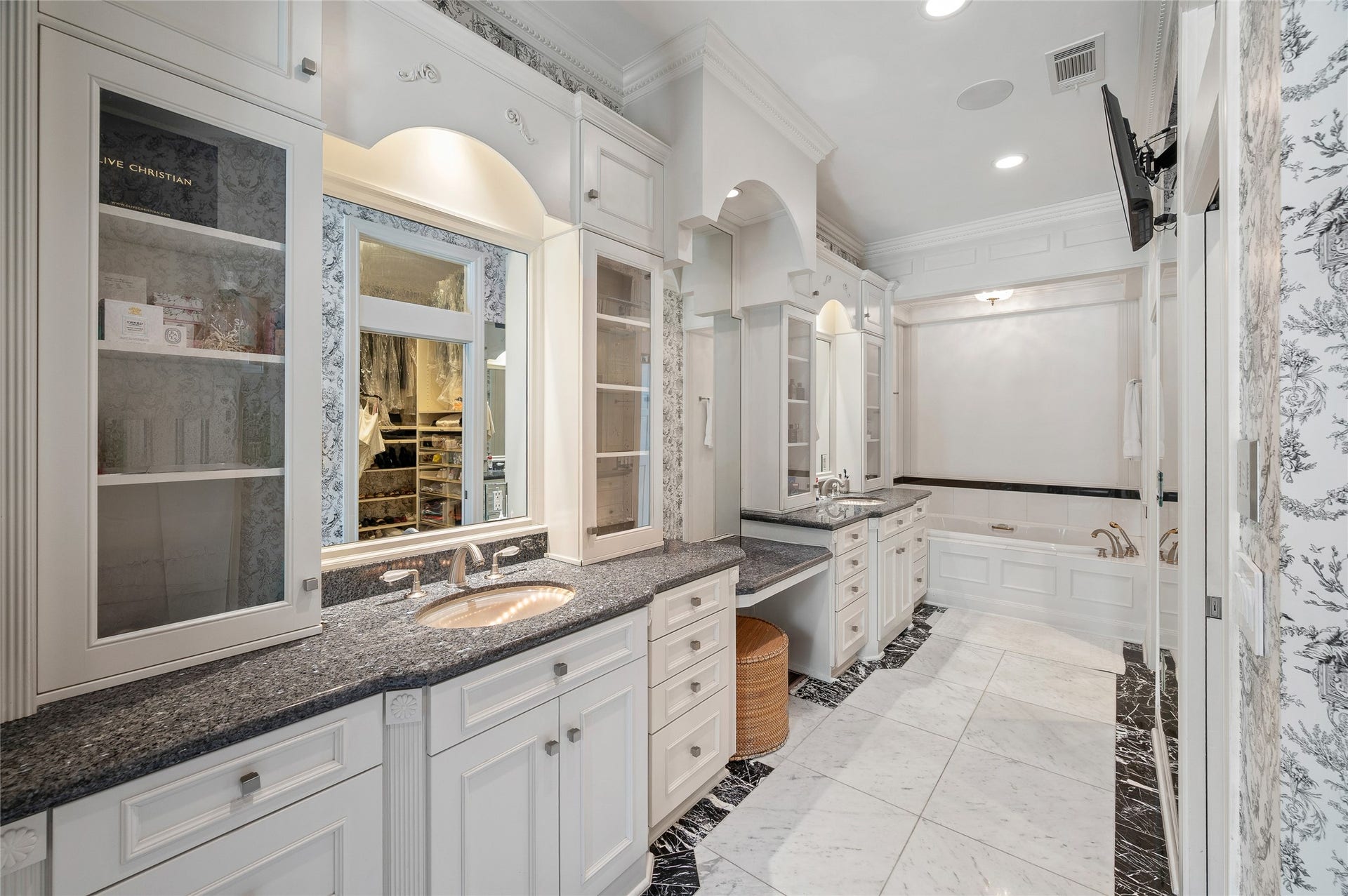 [Primary Bath]
Elegant granite, mirror, and marble finishes enhance the primary bath. Note glass-front upper cabinets, vanity counter, and jetted tu. Interior of the primary closet is reflected in the center mirror.