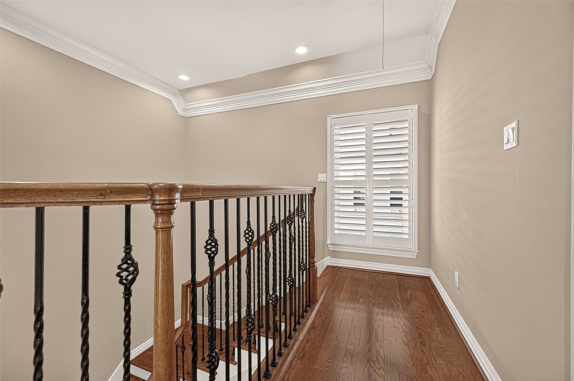 4003 Bellefontaine Street, Houston, TX 77025 Elegant third-floor landing featuring hardwood floors, decorative iron balusters, and detailed crown molding. A tall window with plantation shutters brings natural light into this inviting transition to the bedroom level.