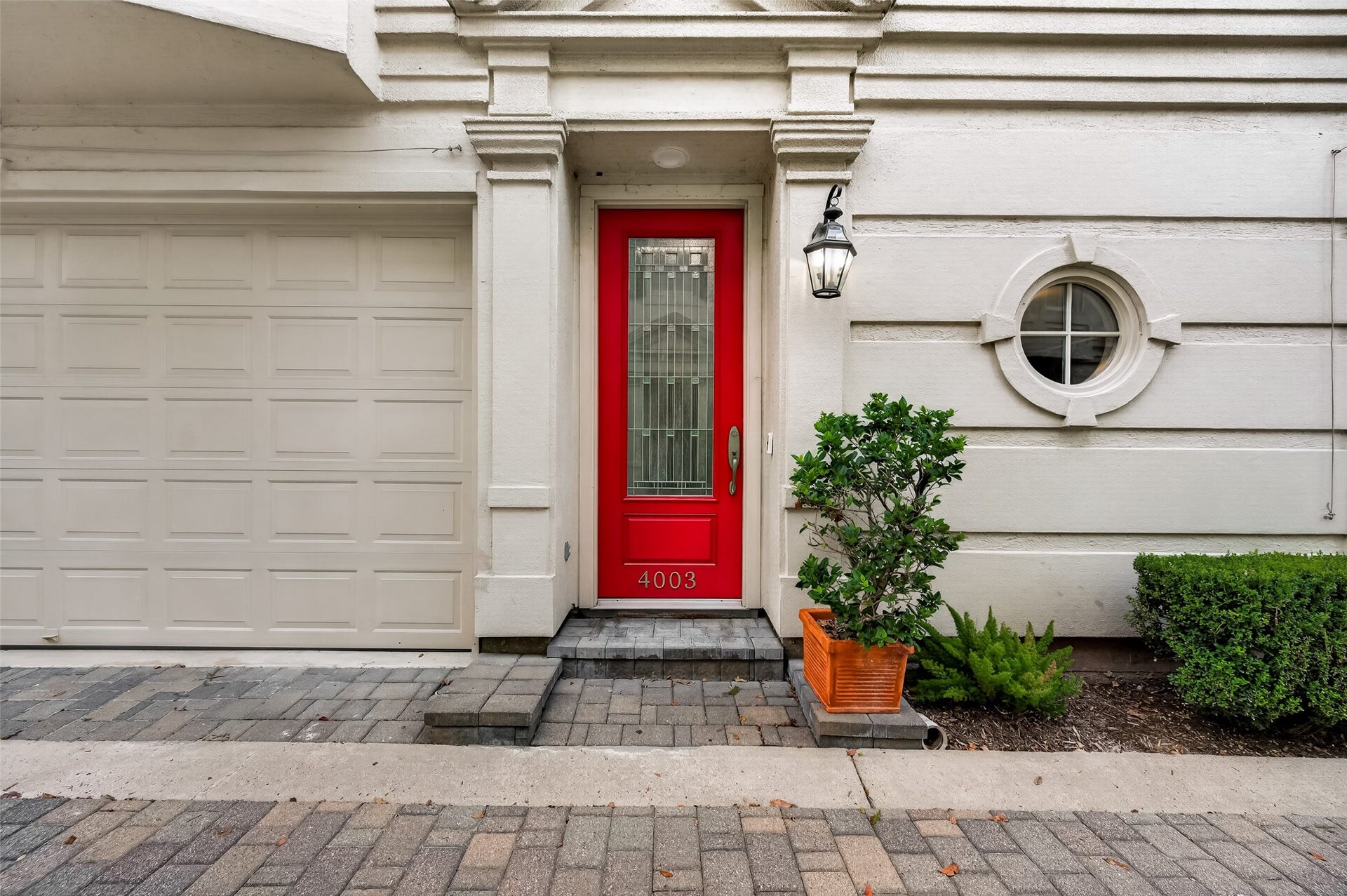4003 Bellefontaine Street, Houston, TX 77025 An inviting entrance featuring a vibrant red door with decorative glass, classic architectural detailing, and a charming round window. Stone pavers and manicured landscaping complete the elegant first impression.