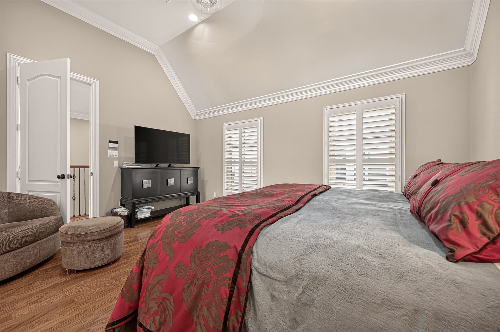 4003 Bellefontaine Street, Houston, TX 77025 Inviting third-floor primary bedroom featuring a soaring vaulted ceiling, detailed crown molding, and rich hardwood floors. Two windows with plantation shutters fill the room with natural light, while a cozy sitting area offers a peaceful spot to unwind.