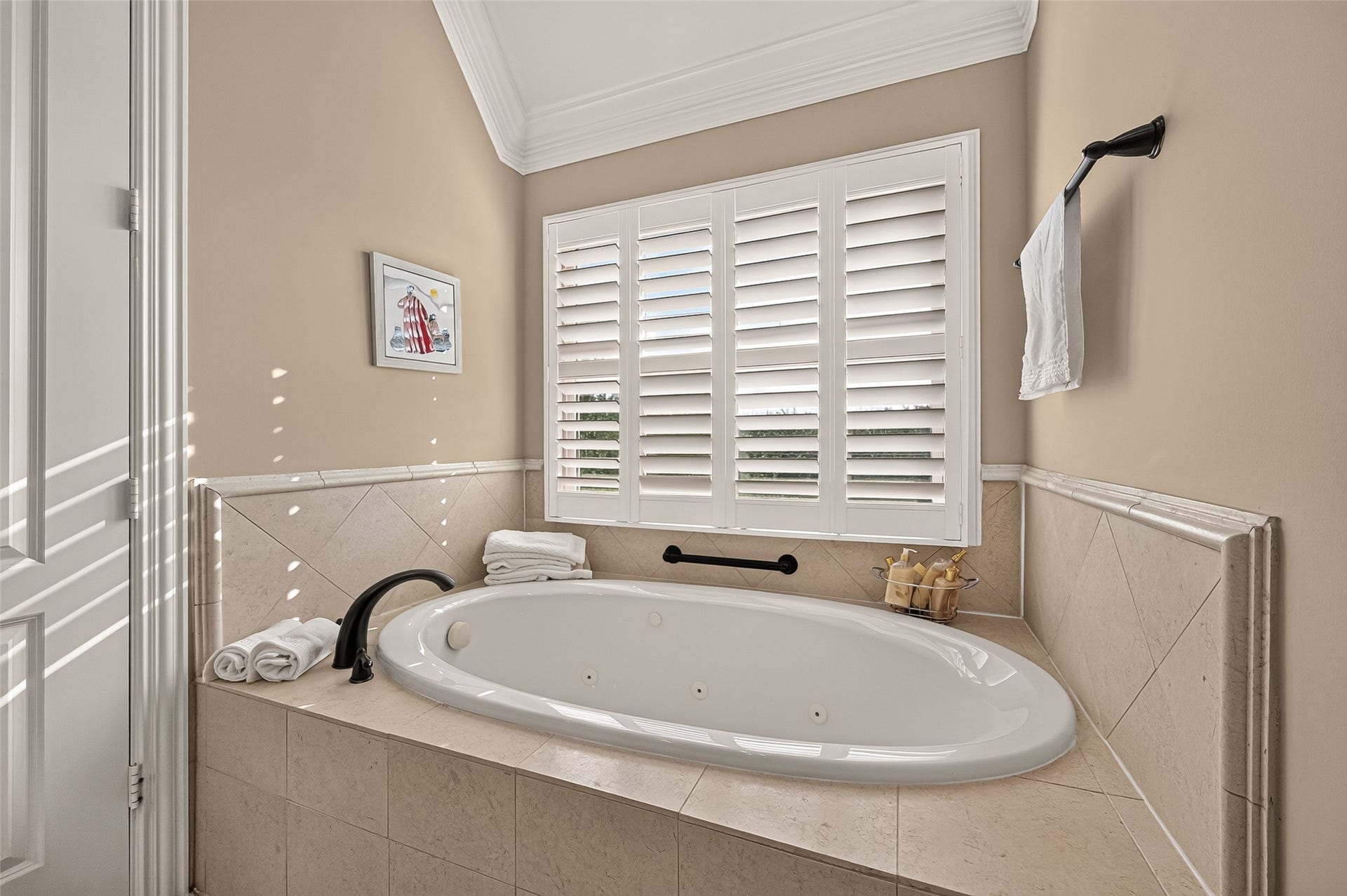 4003 Bellefontaine Street, Houston, TX 77025 Unwind in the primary bathrooms spacious jetted tub, framed by an elegant tile surround and a window with plantation shutters. Detailed crown molding completes this serene setting for relaxation.