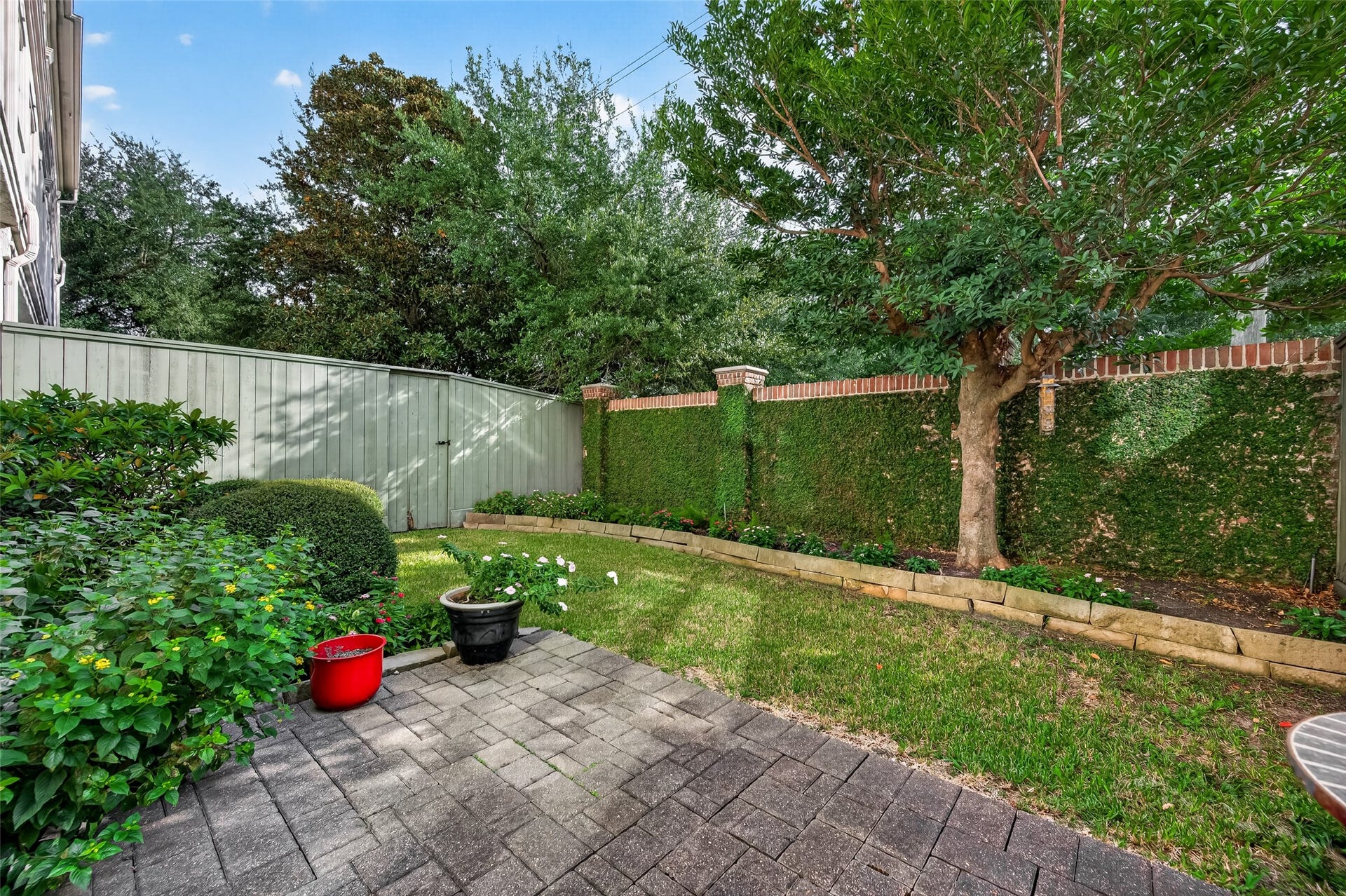 4003 Bellefontaine Street, Houston, TX 77025 Inviting paver patio overlooking a private lawn framed by stone-bordered garden beds, mature trees, and an ivy-covered brick wall. This peaceful outdoor retreat offers a lovely setting for morning coffee, casual gatherings, or quiet relaxation.