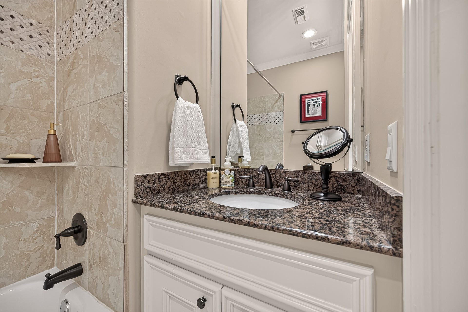 4003 Bellefontaine Street, Houston, TX 77025 Additional view of the third-floor secondary bathroom showcasing a granite vanity, undermount sink, white cabinetry, and a large mirror. The adjacent tub and shower combination features tilework with a decorative mosaic accent.