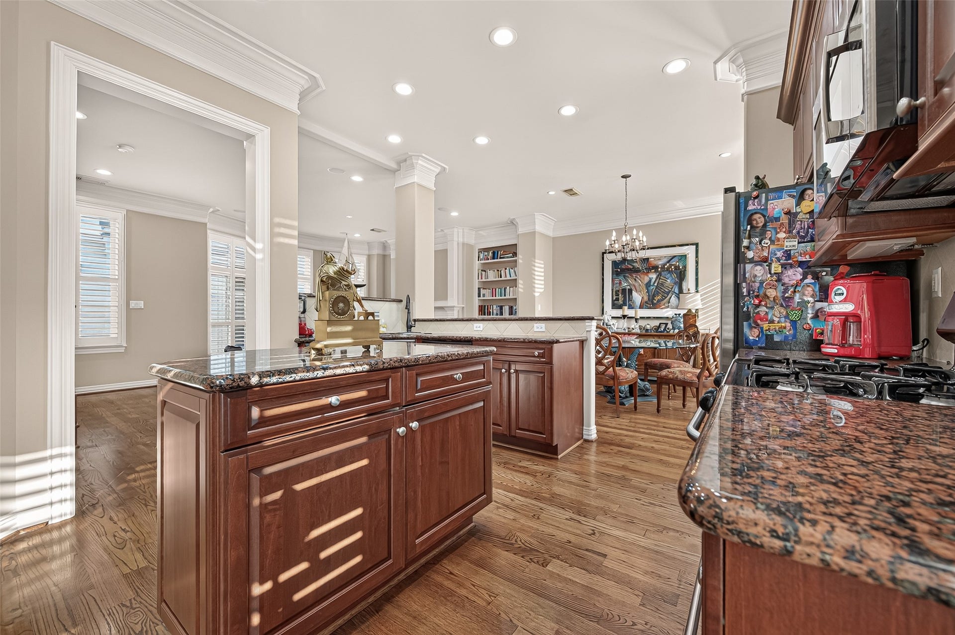 4003 Bellefontaine Street, Houston, TX 77025 Inviting kitchen and breakfast nook featuring a granite-topped island with built-in wine storage, rich wood cabinetry, and a stainless steel gas range. Hardwood floors, crown molding, and plantation shutters create a warm setting for everyday dining.