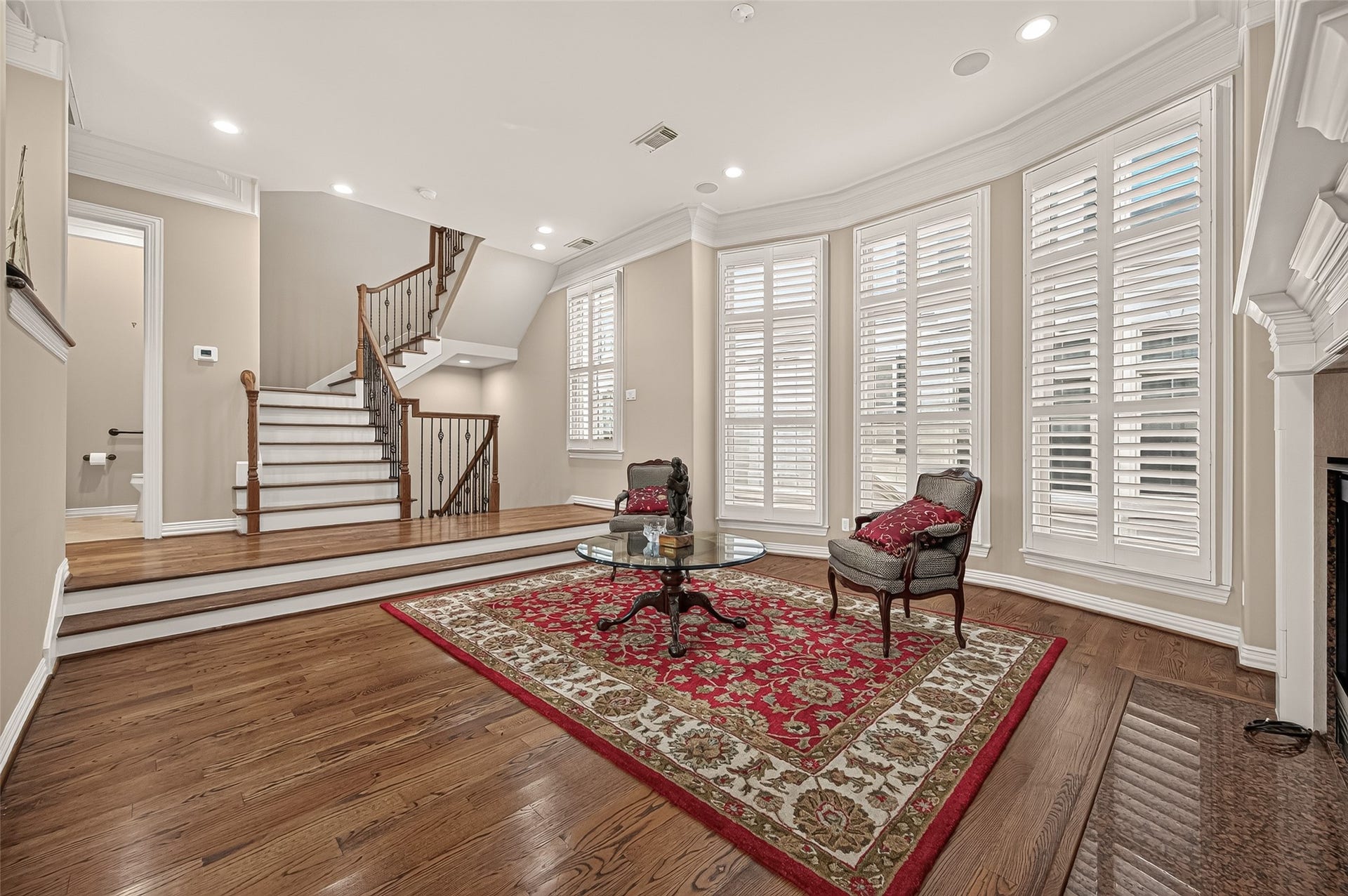 4003 Bellefontaine Street, Houston, TX 77025 Sunlit second-floor living room featuring soaring windows with plantation shutters, rich hardwood floors, and an elegant fireplace. High ceilings, crown molding, and recessed lighting enhance this inviting space for relaxing and entertaining.