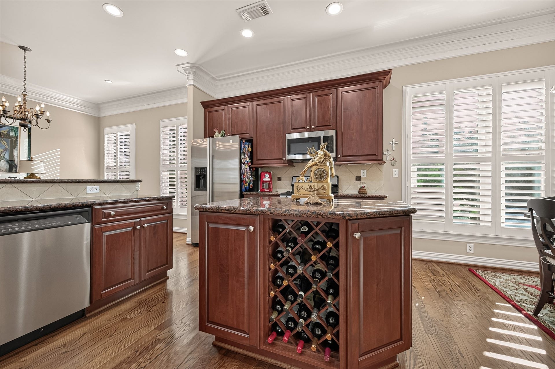 4003 Bellefontaine Street, Houston, TX 77025 Granite-topped kitchen island featuring an integrated wine rack and generous cabinet storage. Rich wood cabinetry, stainless steel appliances, and sunlit windows with plantation shutters create a warm, inviting space for cooking and gathering.