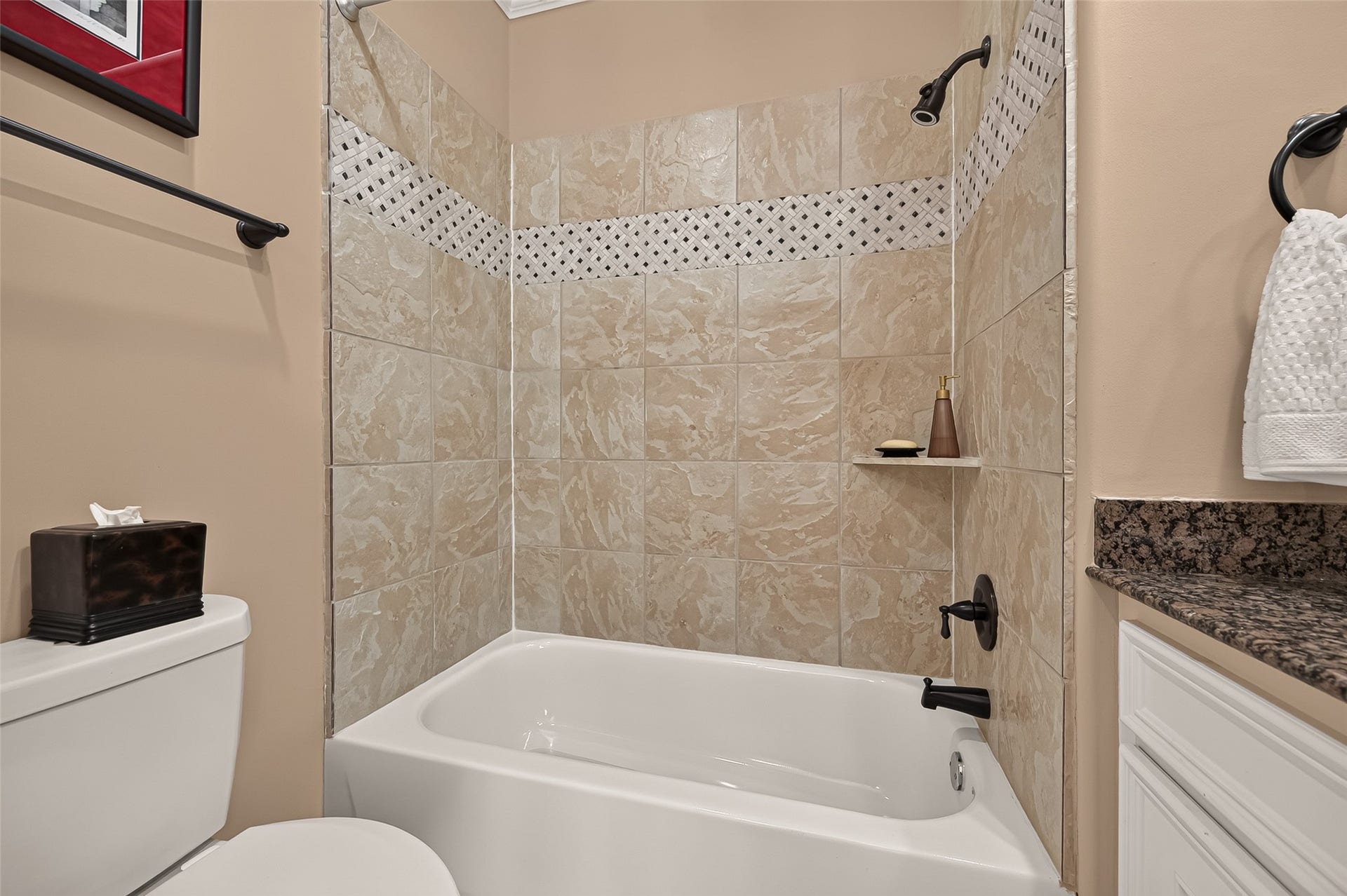 4003 Bellefontaine Street, Houston, TX 77025 Third-floor secondary bathroom featuring a tub and shower combination with a tile surround, decorative mosaic accent, and built-in corner shelf. A granite countertop and classic white cabinetry complete the space.