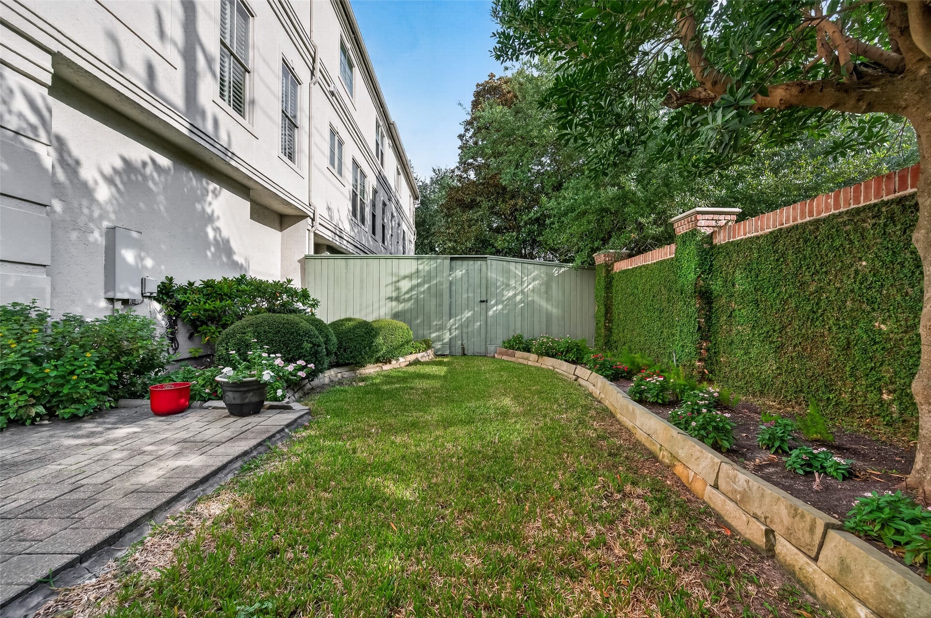 4003 Bellefontaine Street, Houston, TX 77025 Beautifully landscaped private yard featuring a lush lawn, stone-edged flower beds, an ivy-covered brick wall, and a paved patioan inviting setting for outdoor relaxation and entertaining.