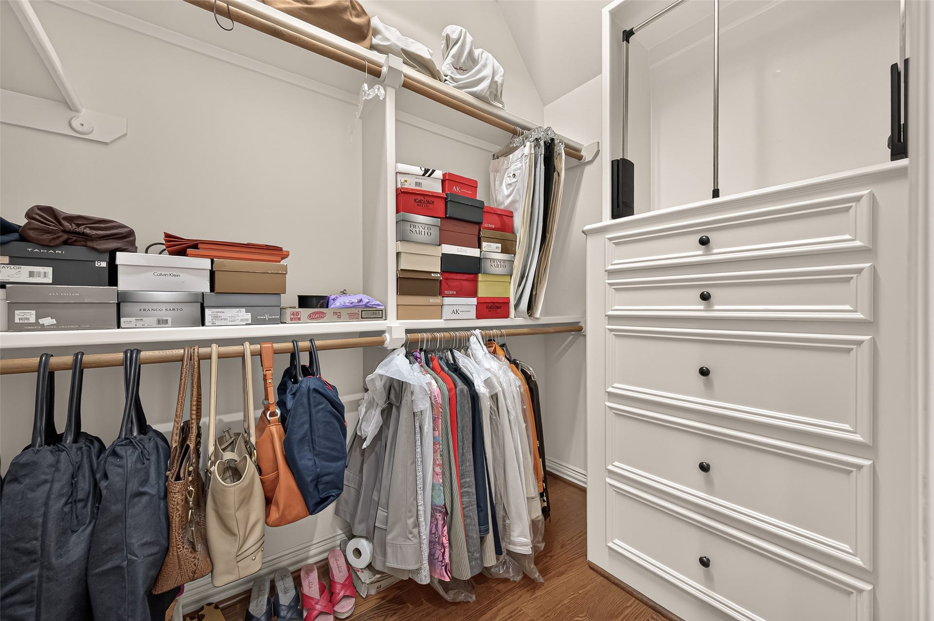 4003 Bellefontaine Street, Houston, TX 77025 One of two walk-in closets in the primary suite, featuring built-in drawers, overhead cabinetry, open shelving, and generous hanging space. Hardwood floors complete this thoughtfully organized wardrobe space.