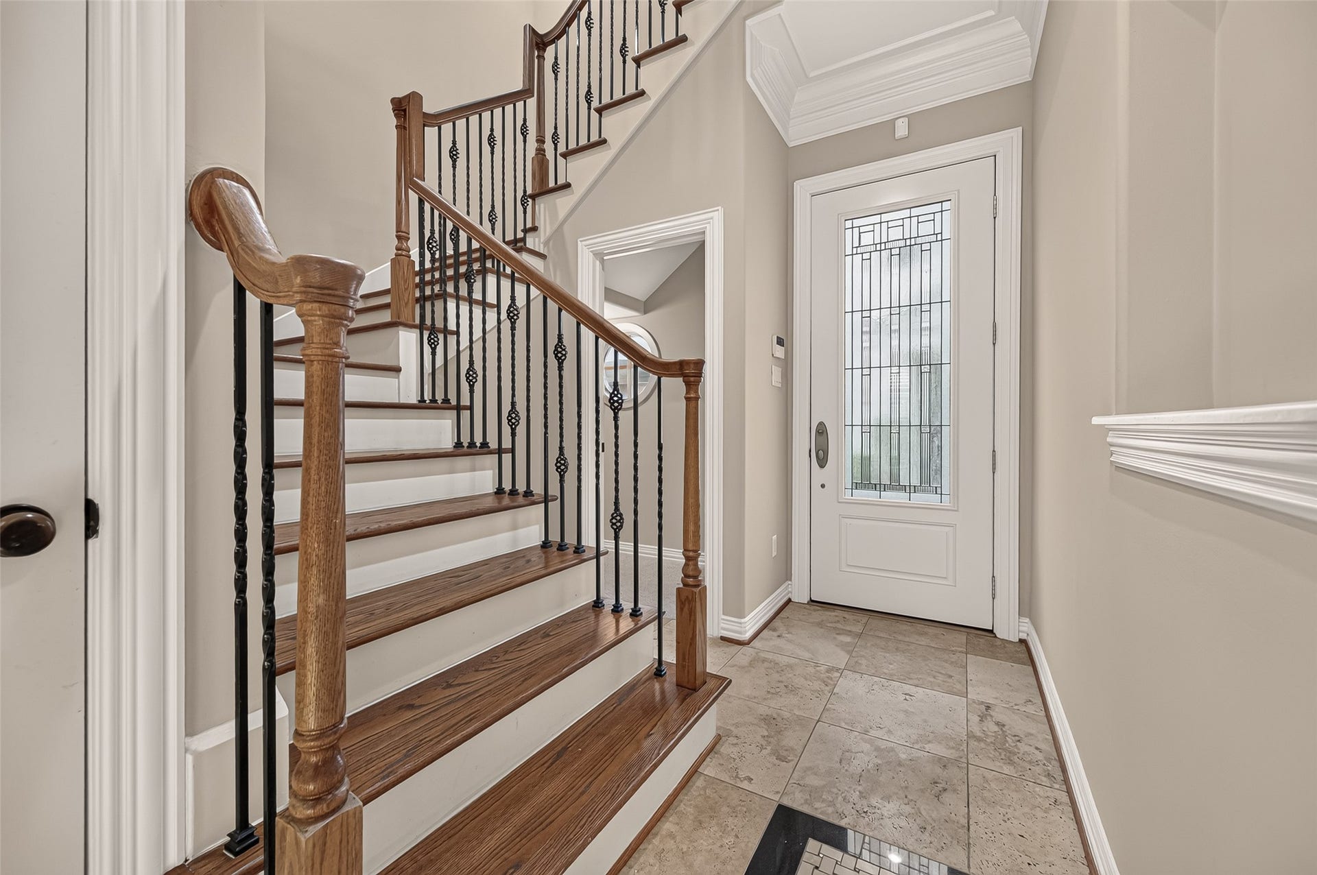 4003 Bellefontaine Street, Houston, TX 77025 Elegant foyer featuring tile flooring, detailed millwork, and a sweeping hardwood staircase with decorative iron balusters. A glass-paneled front door welcomes natural light into this inviting entrance.