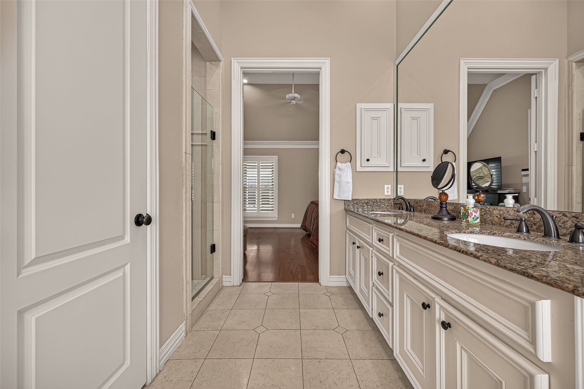 4003 Bellefontaine Street, Houston, TX 77025 Additional view of the primary bathroom showcasing a granite vanity with dual sinks, abundant cabinetry, and an expansive mirror. A separate glass-enclosed shower and tile flooring complete this elegant retreat adjoining the primary bedroom.