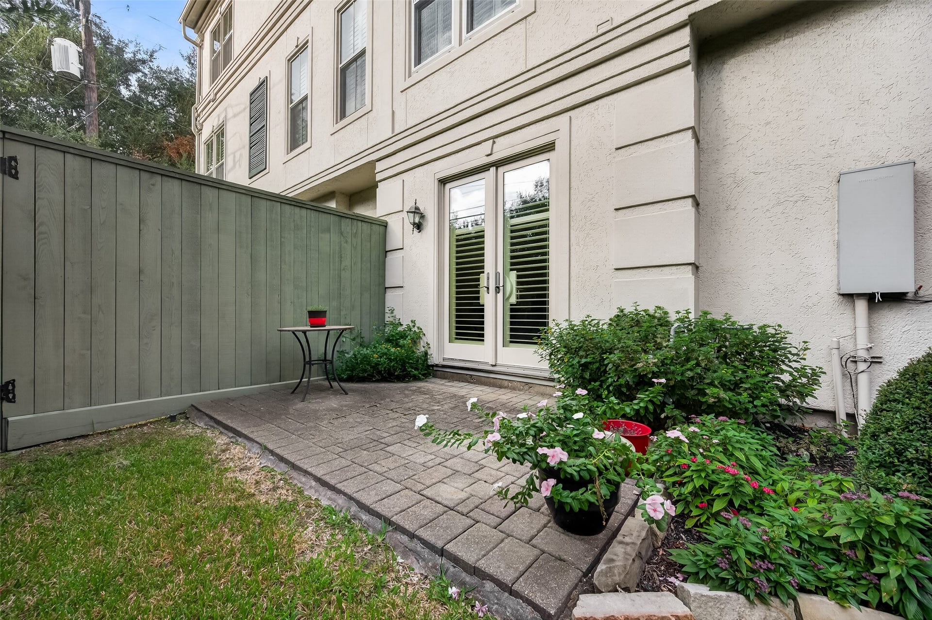 4003 Bellefontaine Street, Houston, TX 77025 Private garden patio featuring stone pavers, flowering plants, and manicured landscaping alongside a grassy yard. Double glass doors connect directly to the first-floor bedroom or office, creating a peaceful spot for morning coffee and outdoor relaxation.