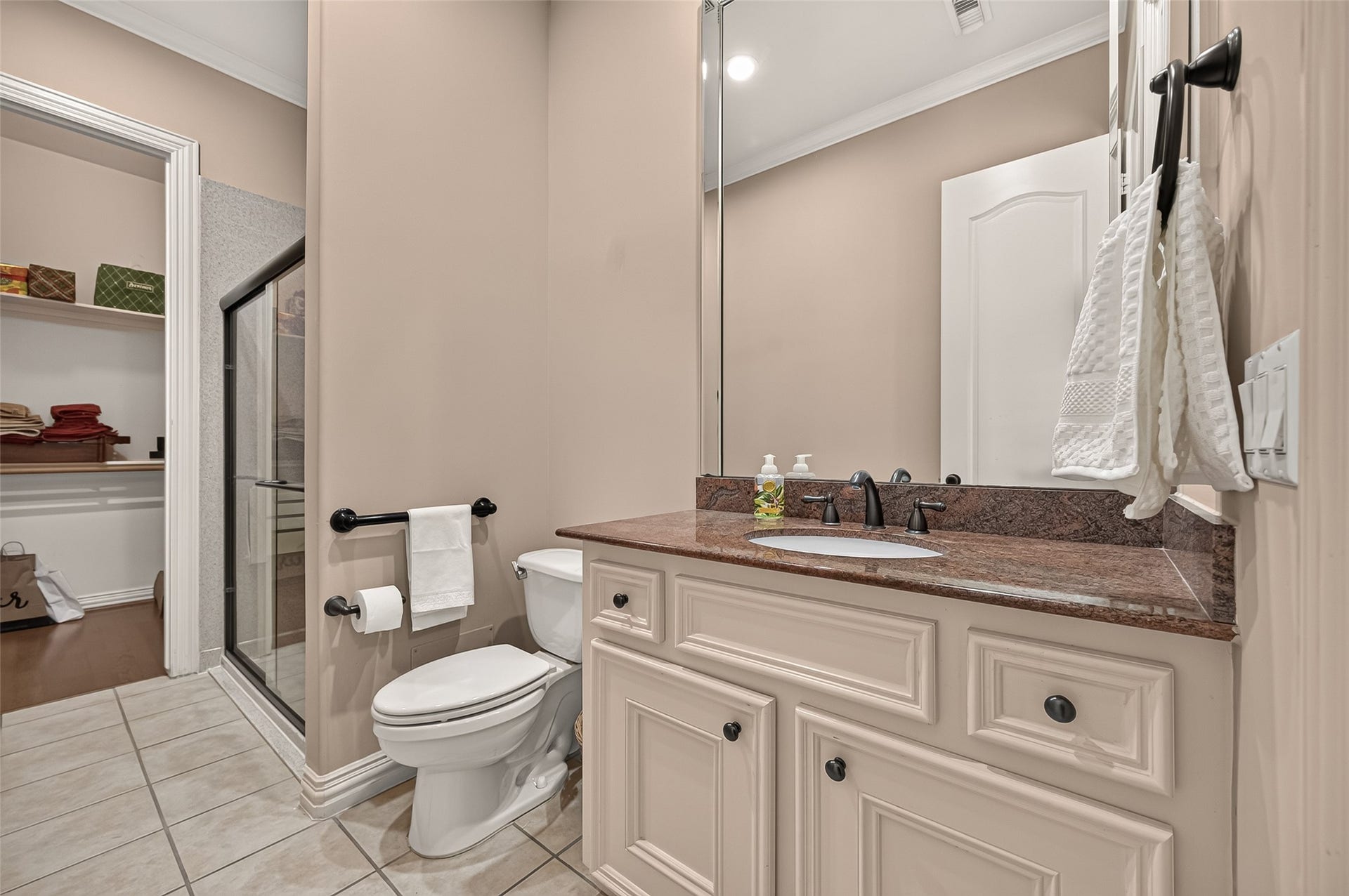 4003 Bellefontaine Street, Houston, TX 77025 Additional view of the first-floor en suite bathroom, highlighting a generous vanity with ample cabinetry, a large mirror, and a glass-enclosed shower. The adjoining walk-in closet provides convenient storage.