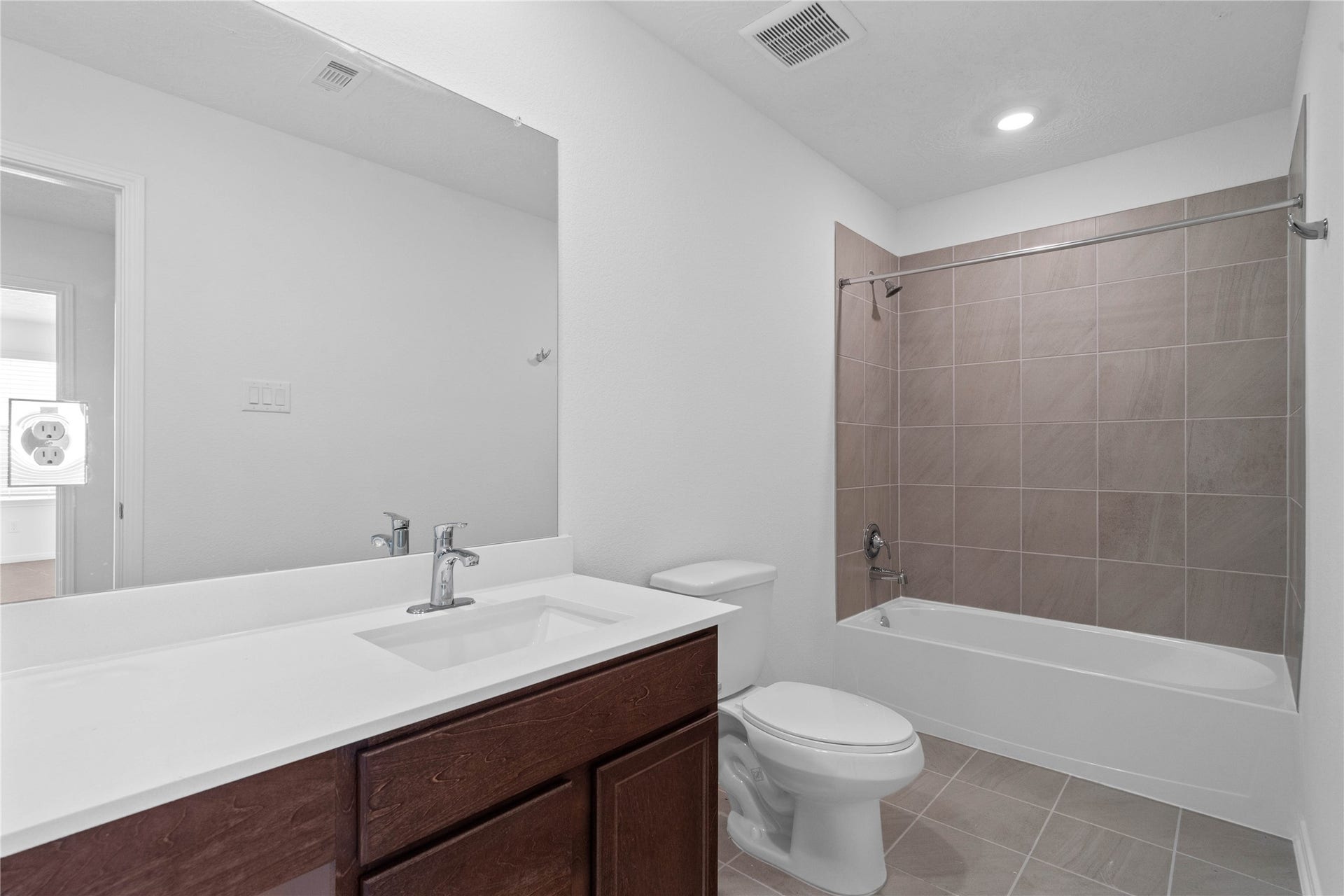The secondary bathroom showcases tile flooring, a bath/shower combo with Daltile tile surround, a vanity with knee space and stunning light countertop, a mirror, sleek fixtures, and contemporary finishes throughout.