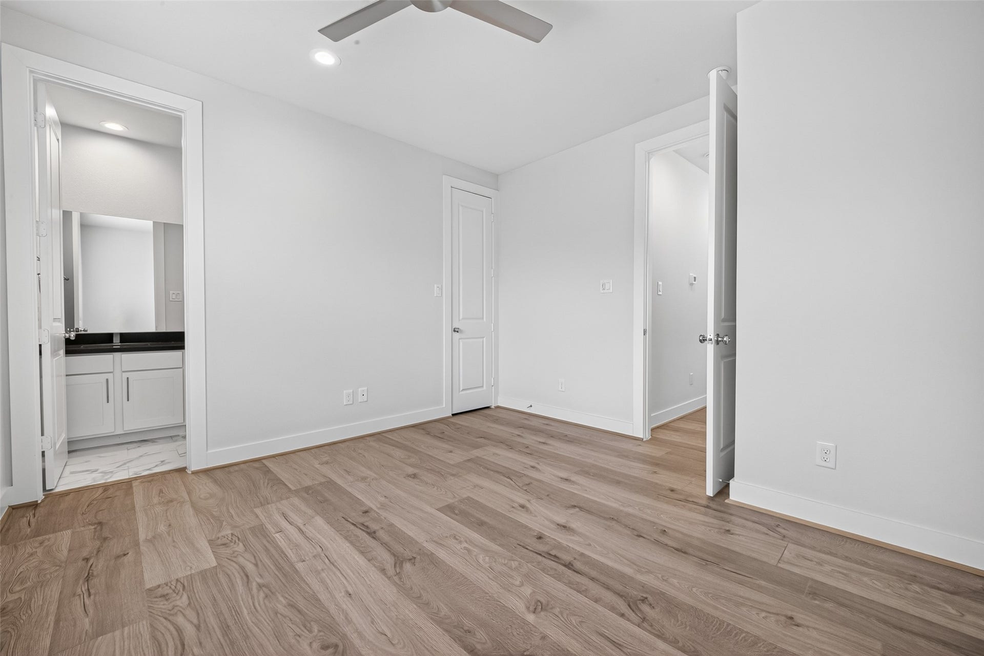 Bright and spacious secondary bedroom featuring elegant Swiss wood like flooring, a ceiling fan, and an ensuite bathroom for added convenience.