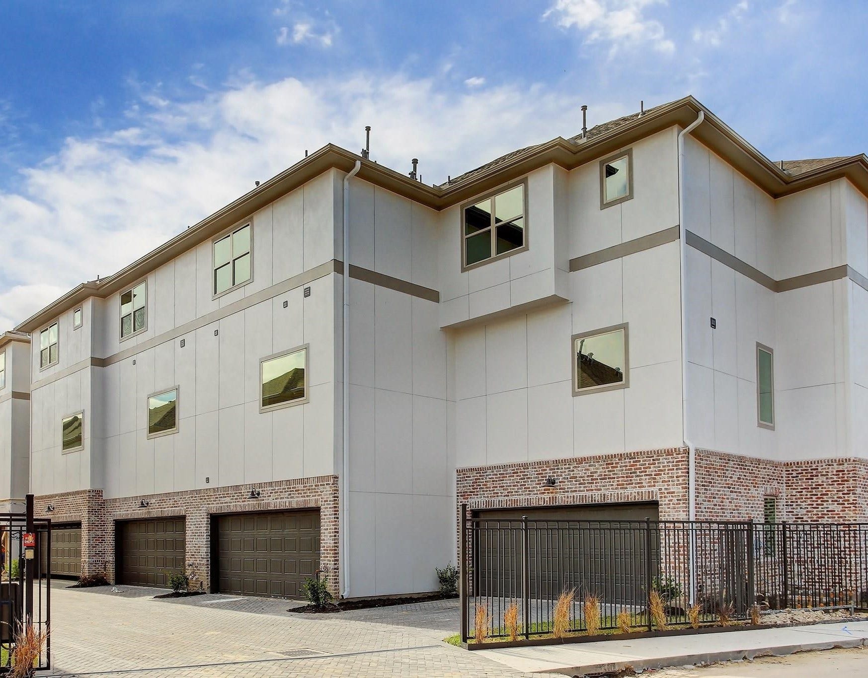 Modern multi-story townhomes with brick accents and spacious garages, situated in a gated community for added security and privacy.