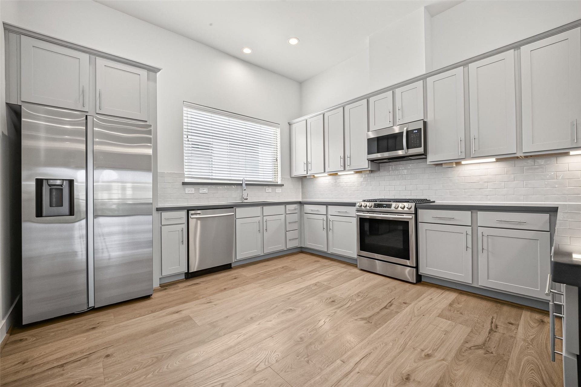 Modern kitchen with sleek stainless steel appliances, light gray cabinetry, and elegant Swiss flooring, offering a bright and spacious cooking area.