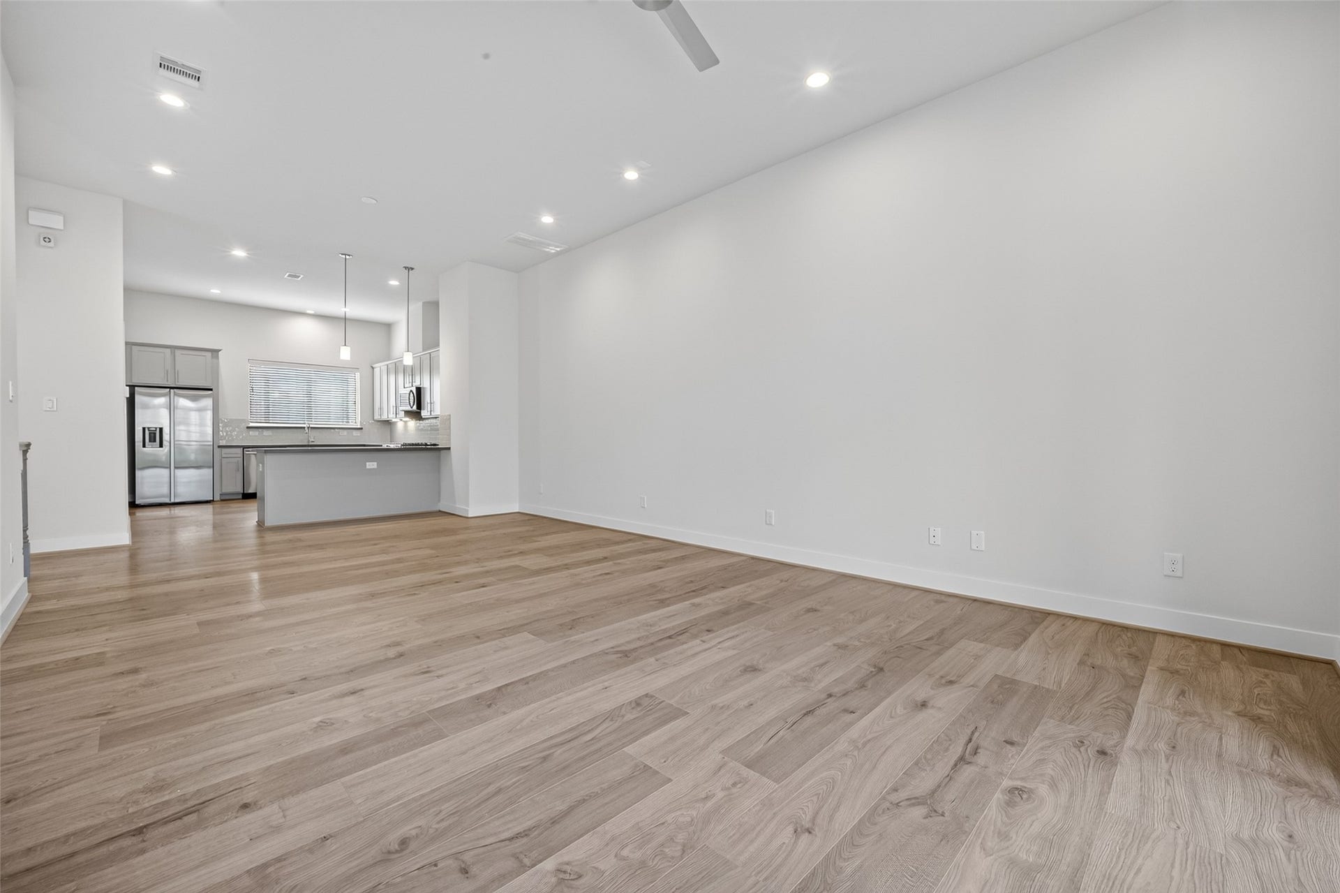 Spacious open-concept living area with sleek LVP floors flowing into a modern kitchen featuring stainless steel appliances and a large island, perfect for entertaining.